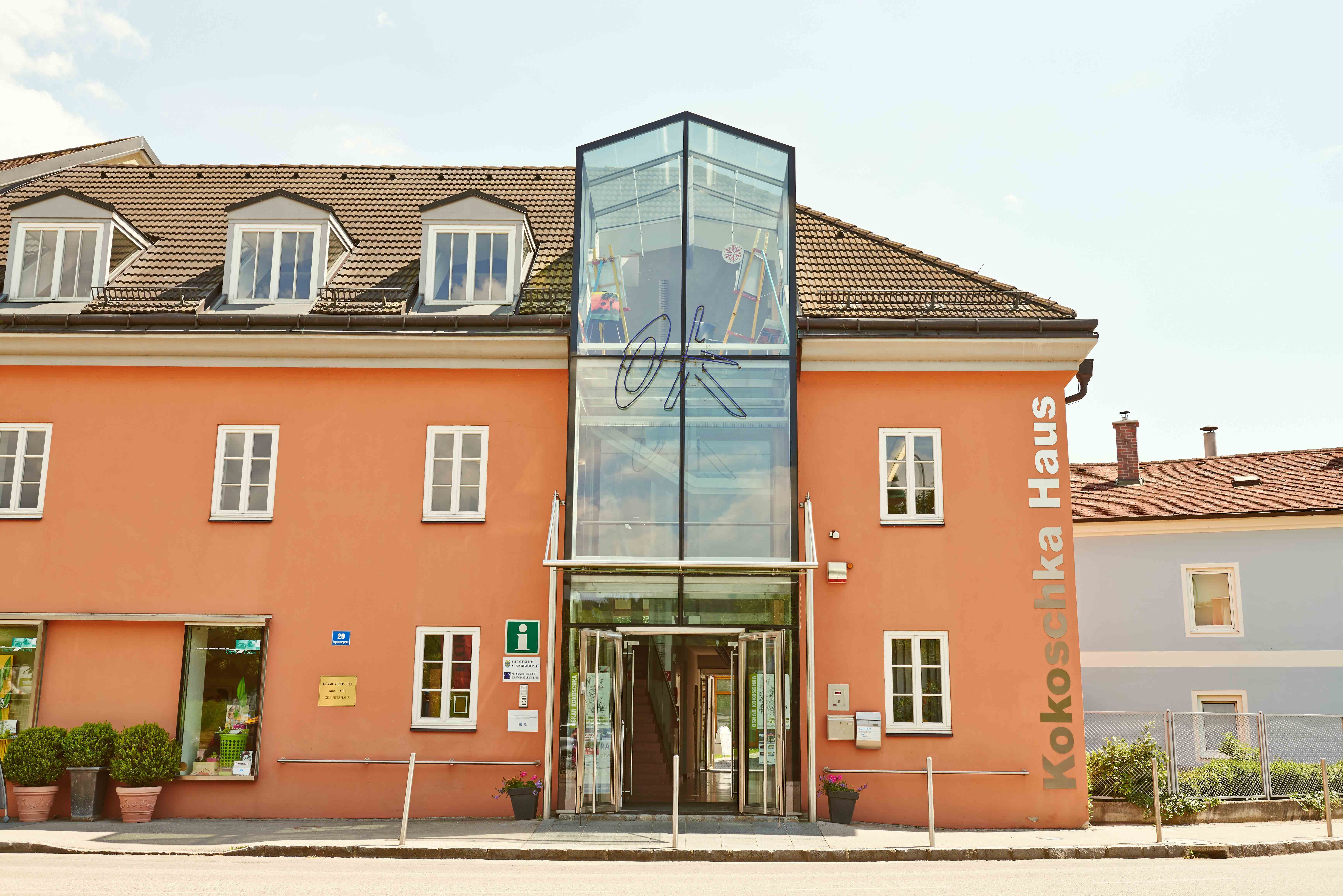 Das Oskar Kokoschkahaus mit orangefarbener Fassade und gläsernem Eingang.