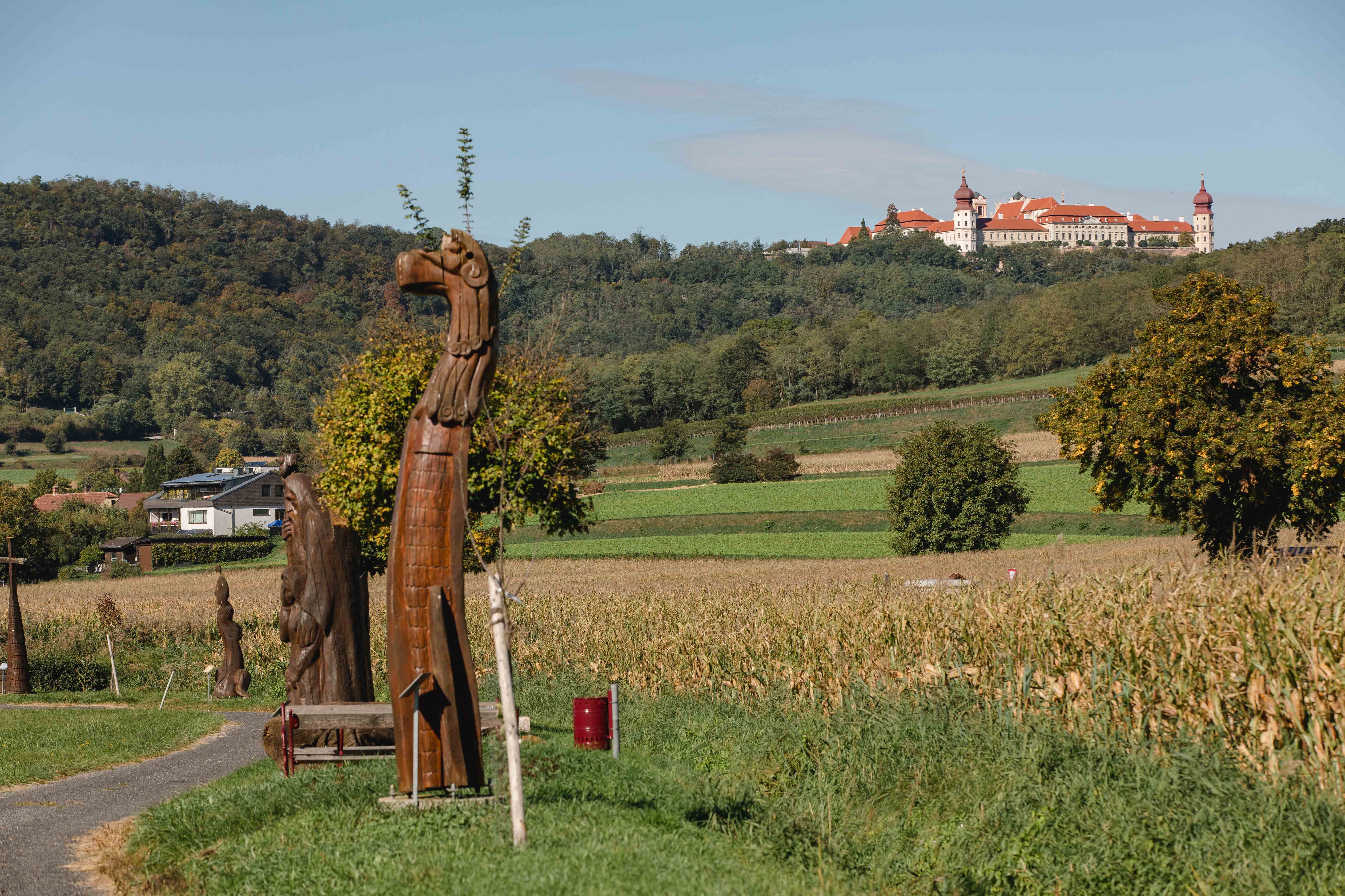 Skulpturenweg mit Holzskulpturen und Blick auf Stift Göttweig in der Ferne.