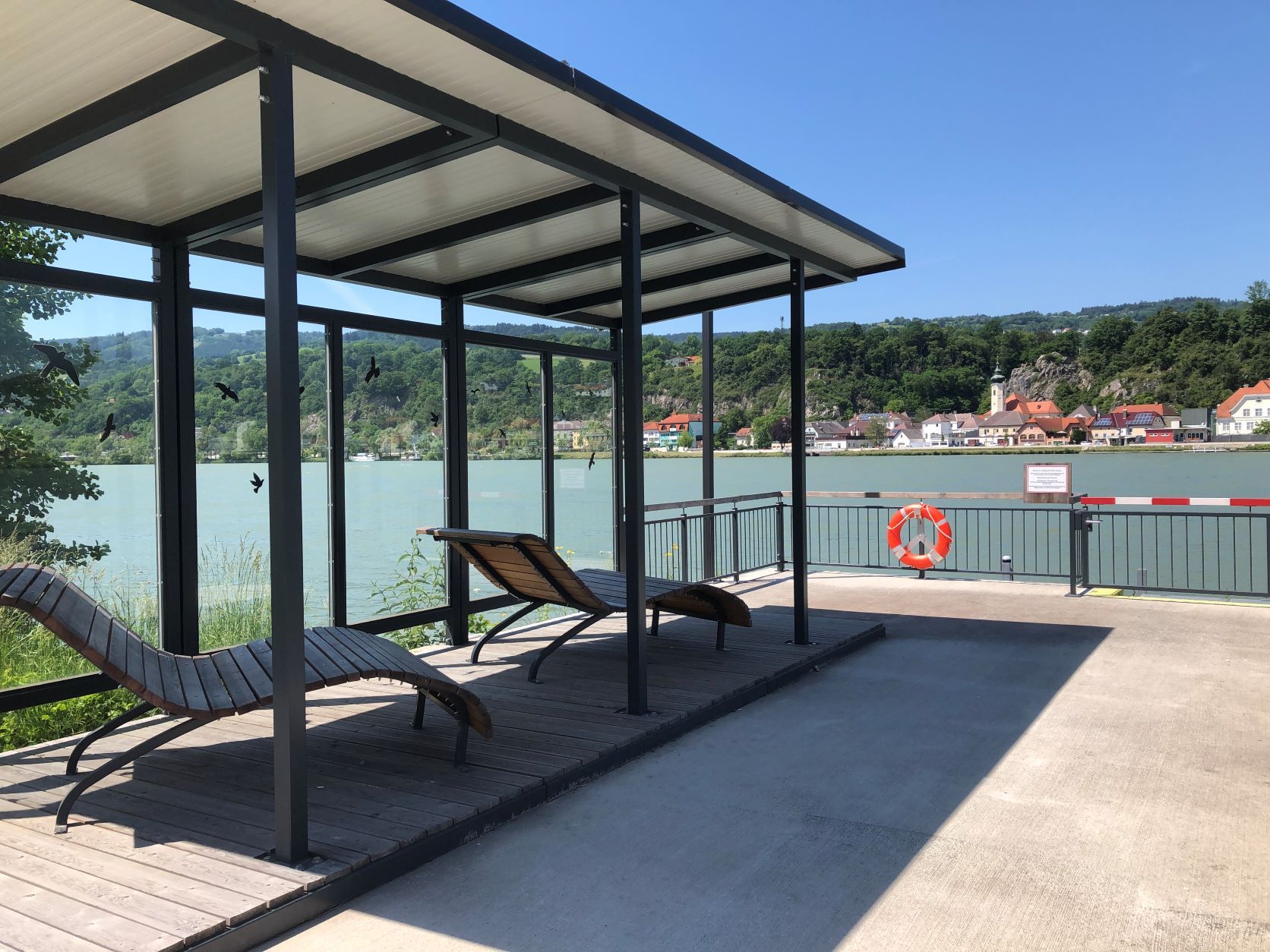Anlegestelle mit Liegestühlen und Blick auf Fluss und Dorf.