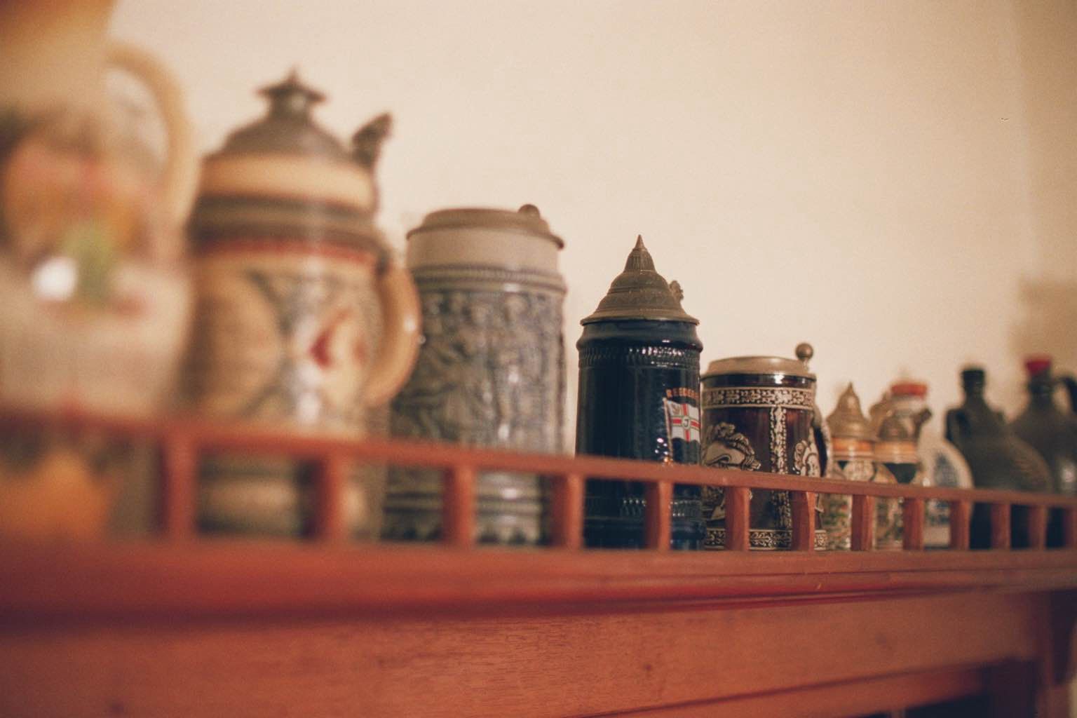 Eine Sammlung von Bierkrügen auf einem Holzregal, unscharf im Vordergrund.