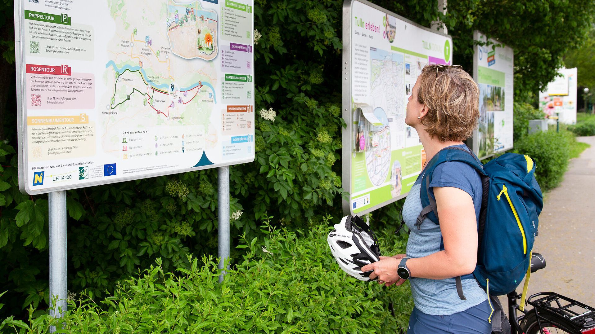 Frau liest auf Infotafel mit Helm in der Hand.