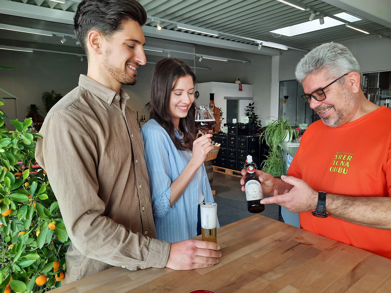 Three people are standing at a table tasting beer in a brewery.