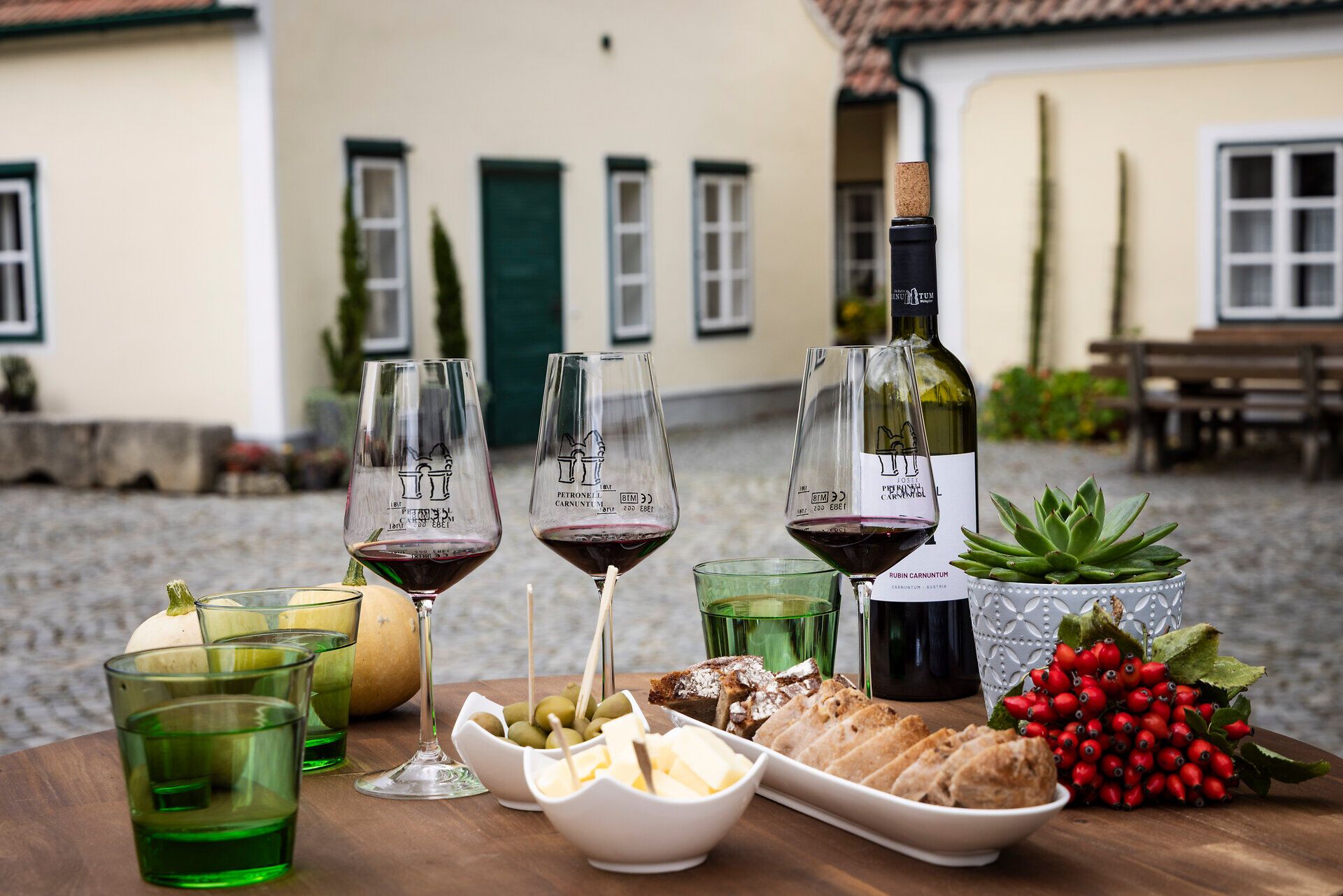 Rotweingläser, Brot, Oliven und Käsewürfel auf einem Holztisch. 