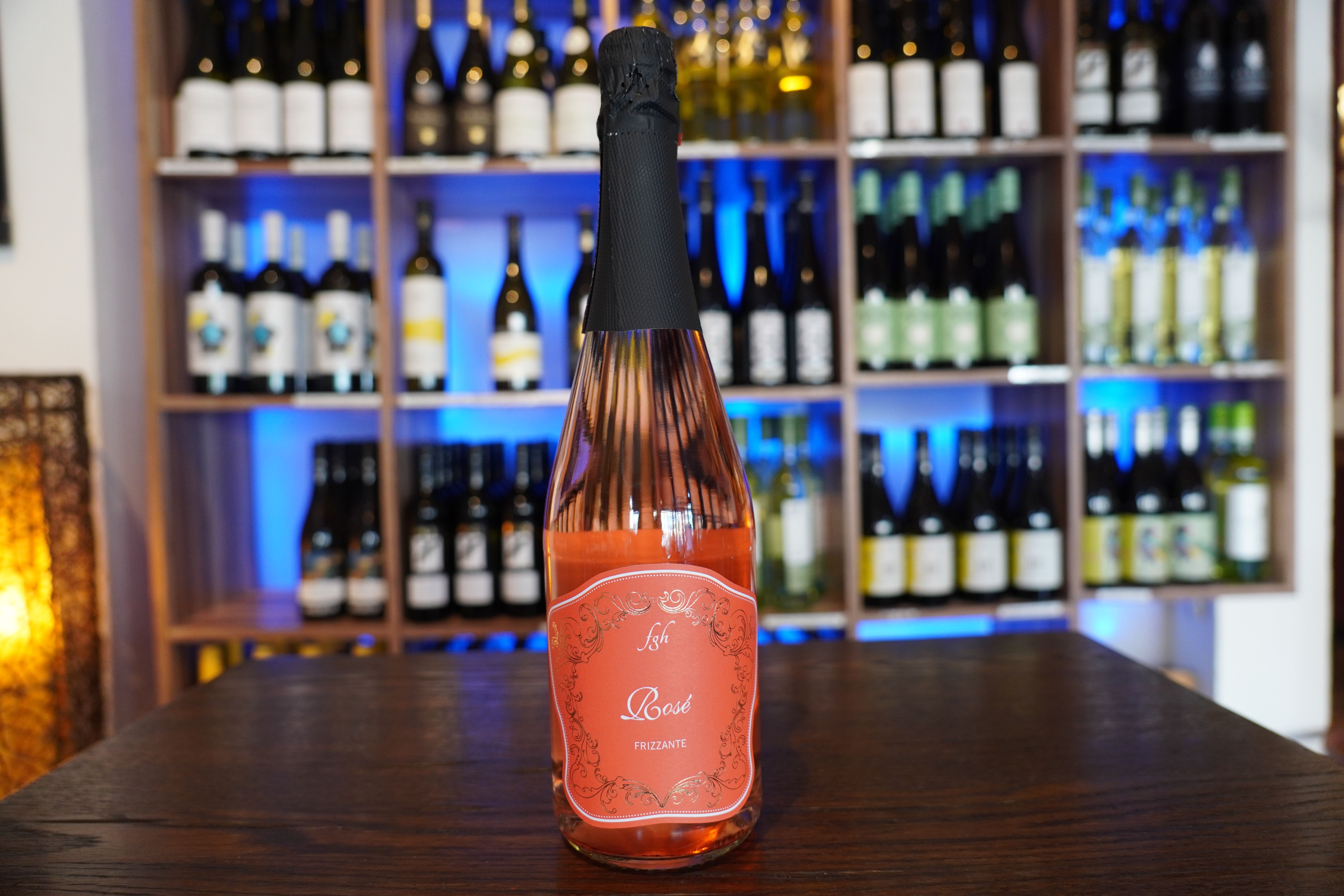 Eine Roséweinflasche steht auf einem Tisch vor einem Weinregal.