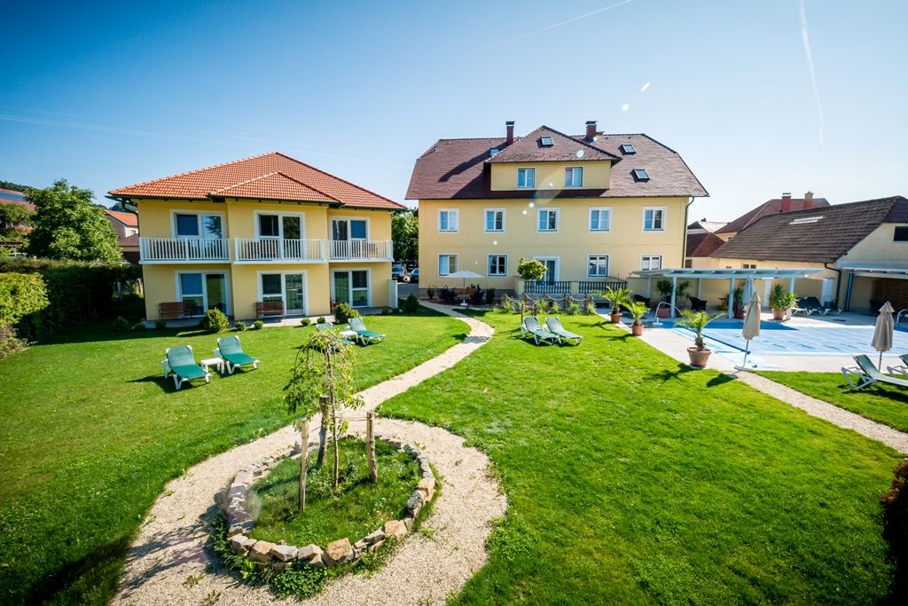 Gartenanlage mit gelben Gebäuden und Liegestühlen bei sonnigem Wetter.