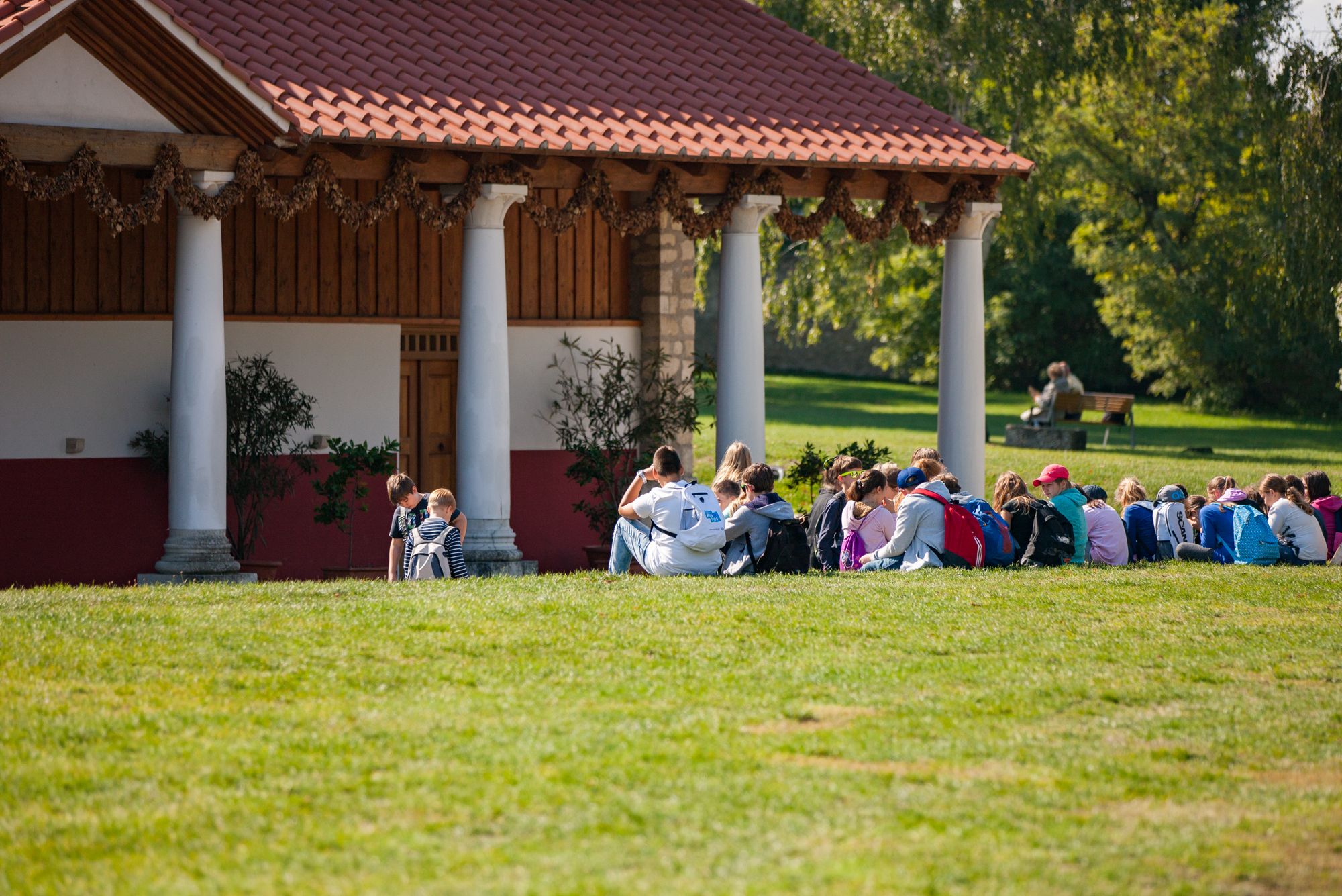 Schulklasse sitzt in der Wiese vor einer Römischen Therme in der Römerstadt Carnuntum