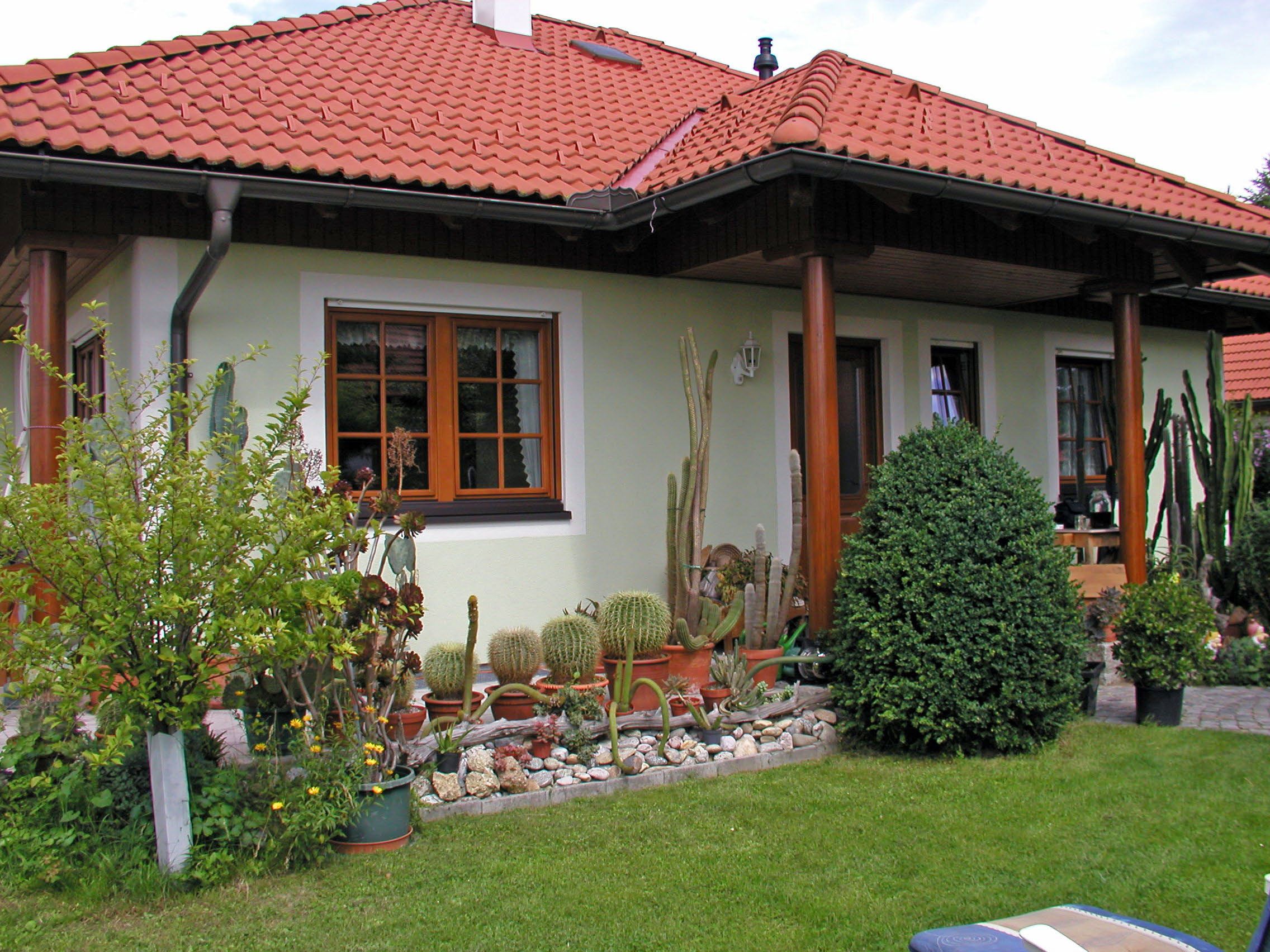 Dom s červenou škridlovou strechou, obklopený záhradou s kaktusmi a kríkmi.