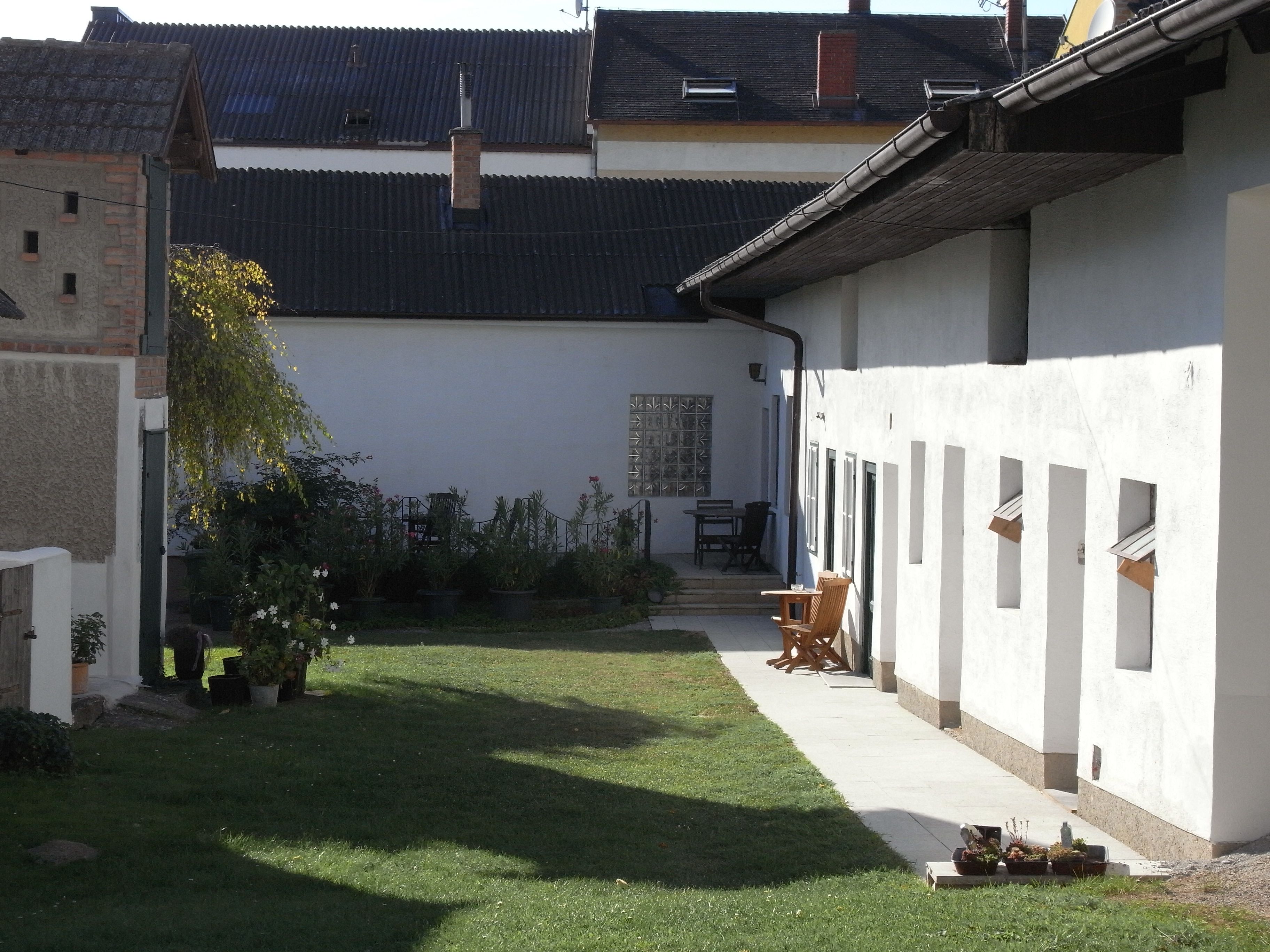 Hof mit Rasenfläche, weißen Gebäuden und Gartenmöbeln.