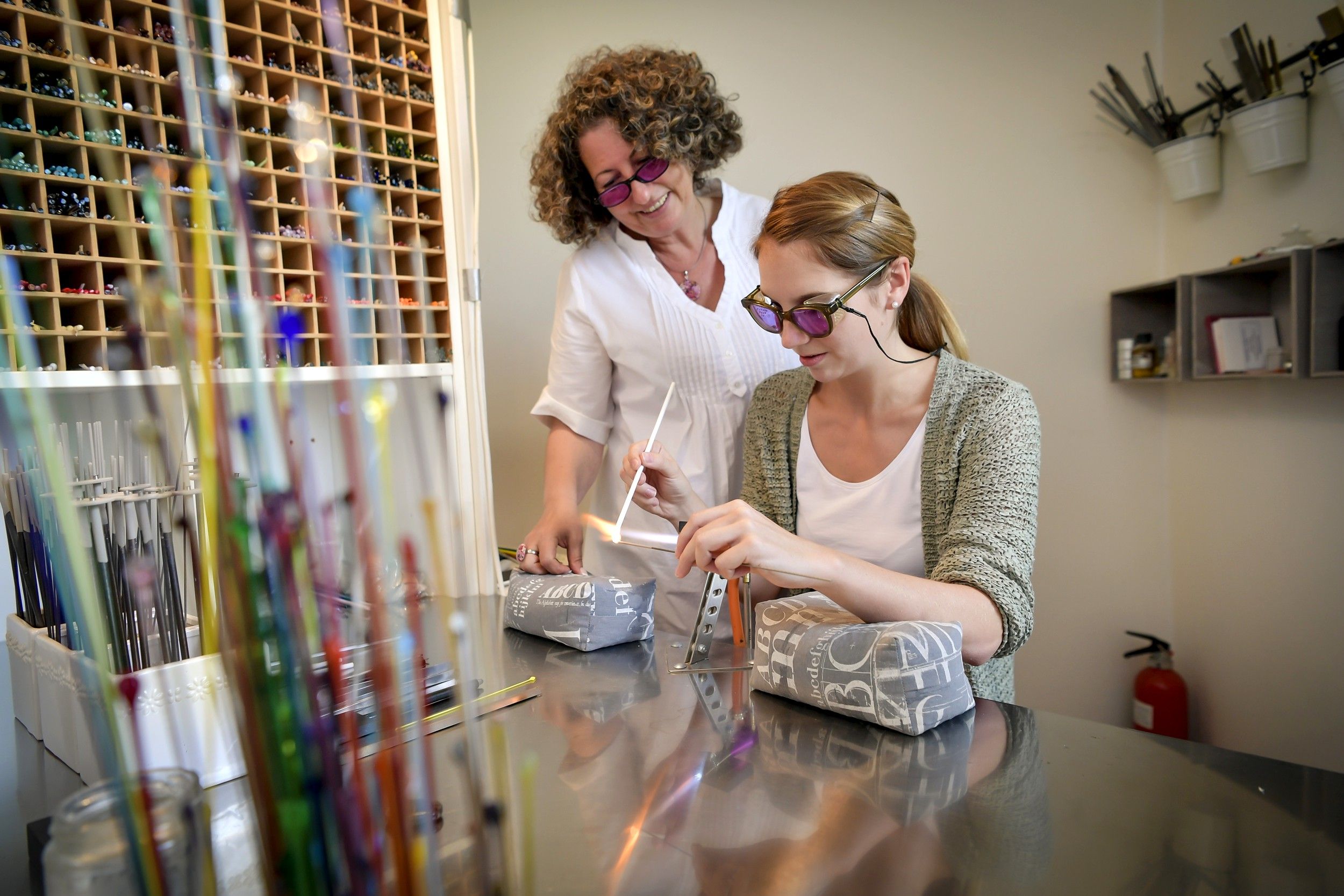 Zwei Frauen arbeiten mit Glasstäben in einer Werkstatt.