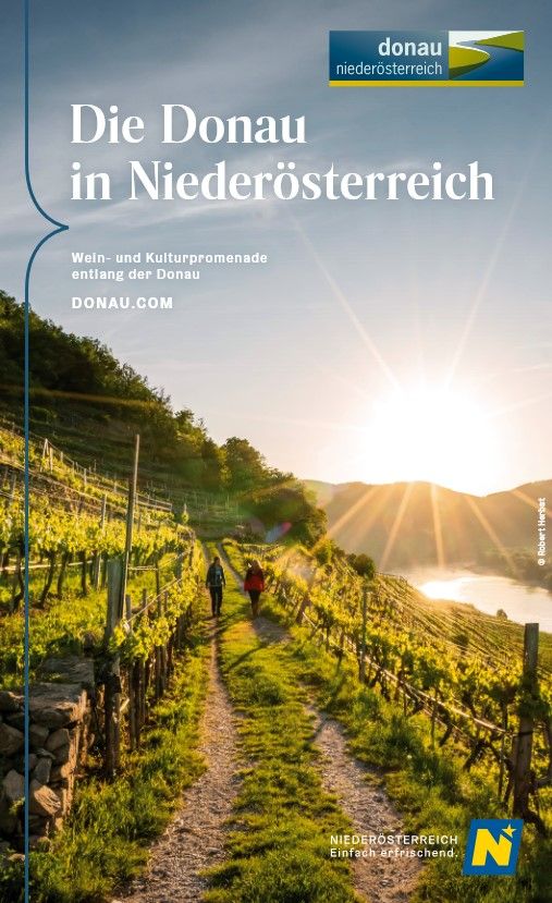 Zwei Frauen wandern entlang eines Feldweges umgeben von Weingärten in der Wachau. Im Hintergrund sieht man die Donau.