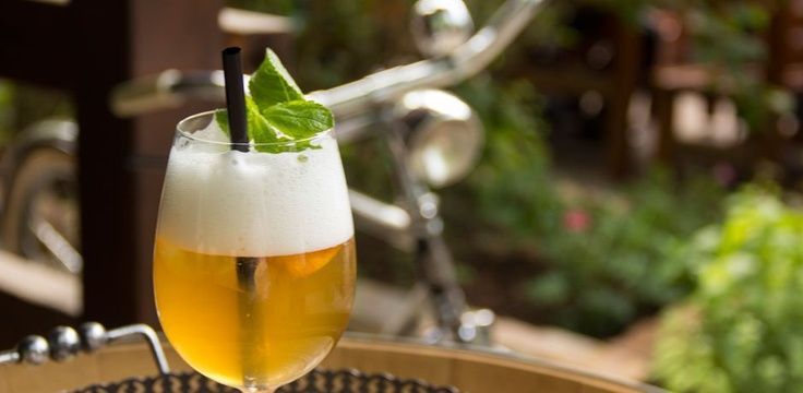 Ein Glas mit Schaumgetränk und Minzblatt auf einem Tisch im Freien, im Hintergrund ein Fahrrad.