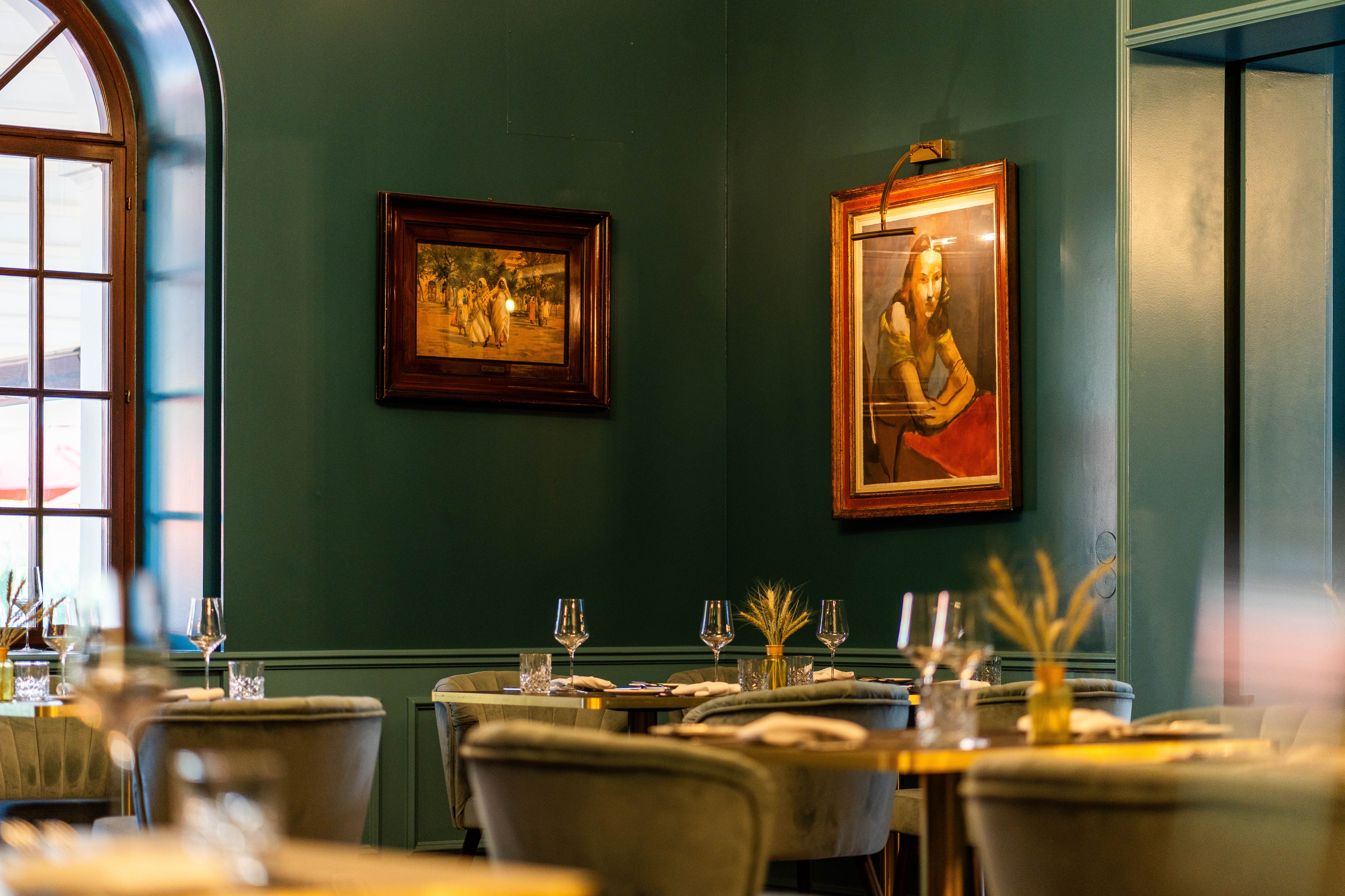 Interiér hotelu a restaurace Grafenegg s prostřenými stoly, zelenými stěnami, velkými okny a zarámovanými obrazy.