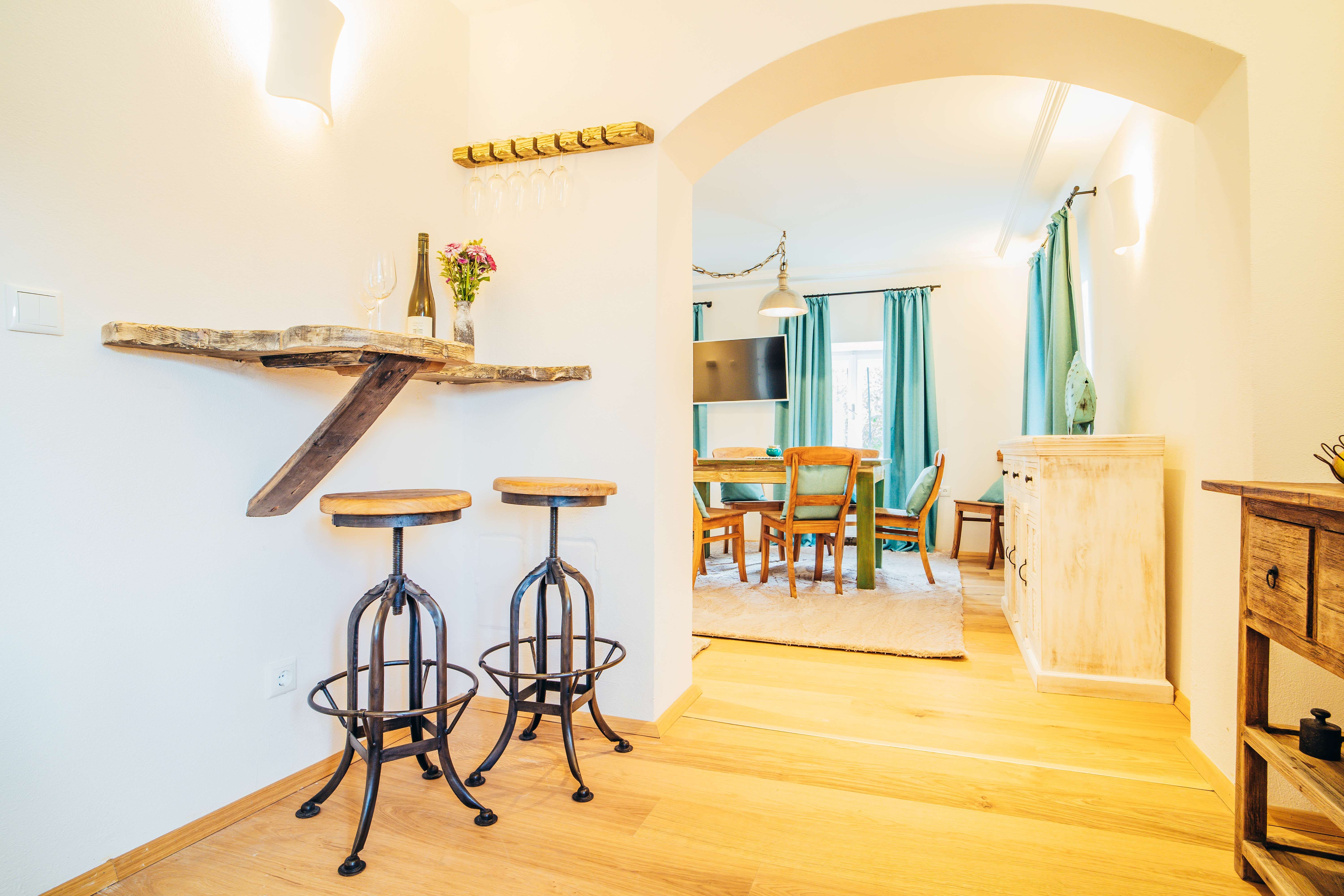 Gemütliches Wohnzimmer mit Holzmöbeln, Barhockern und Esstisch.