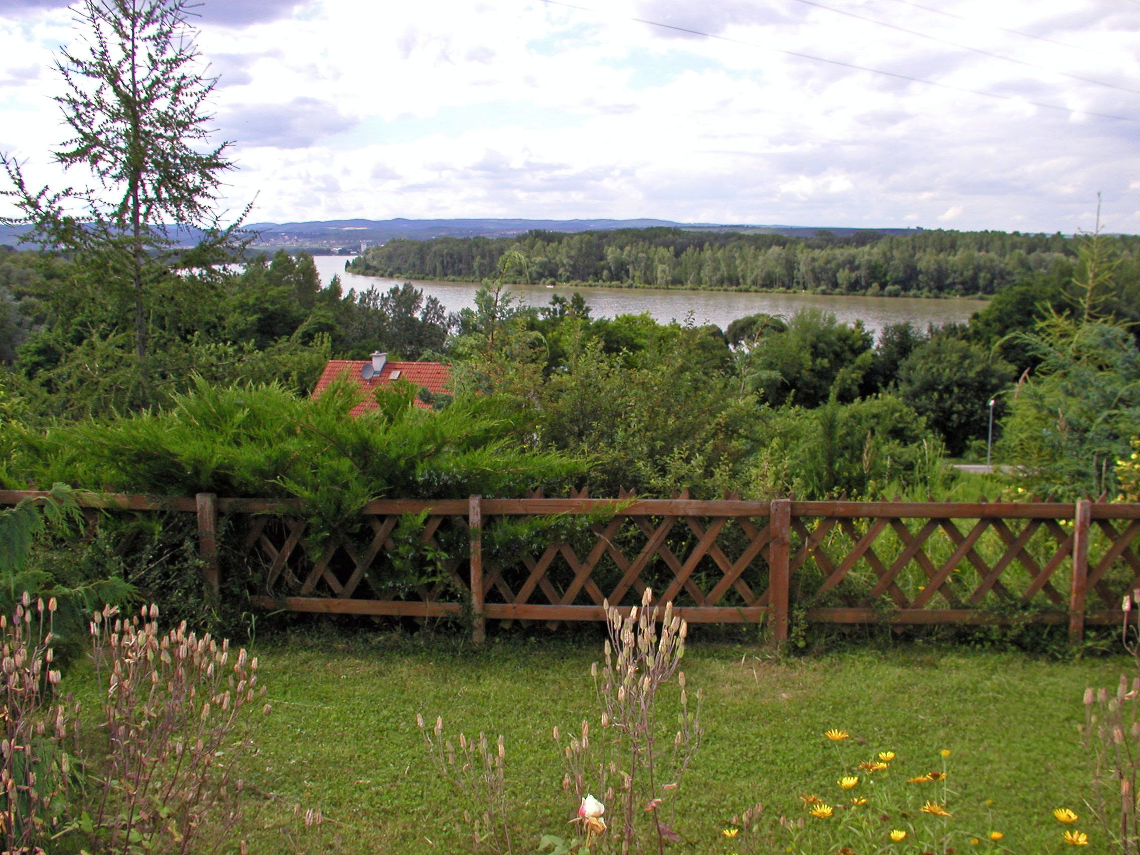 Krajina s riekou, stromami a dreveným plotom v popredí.