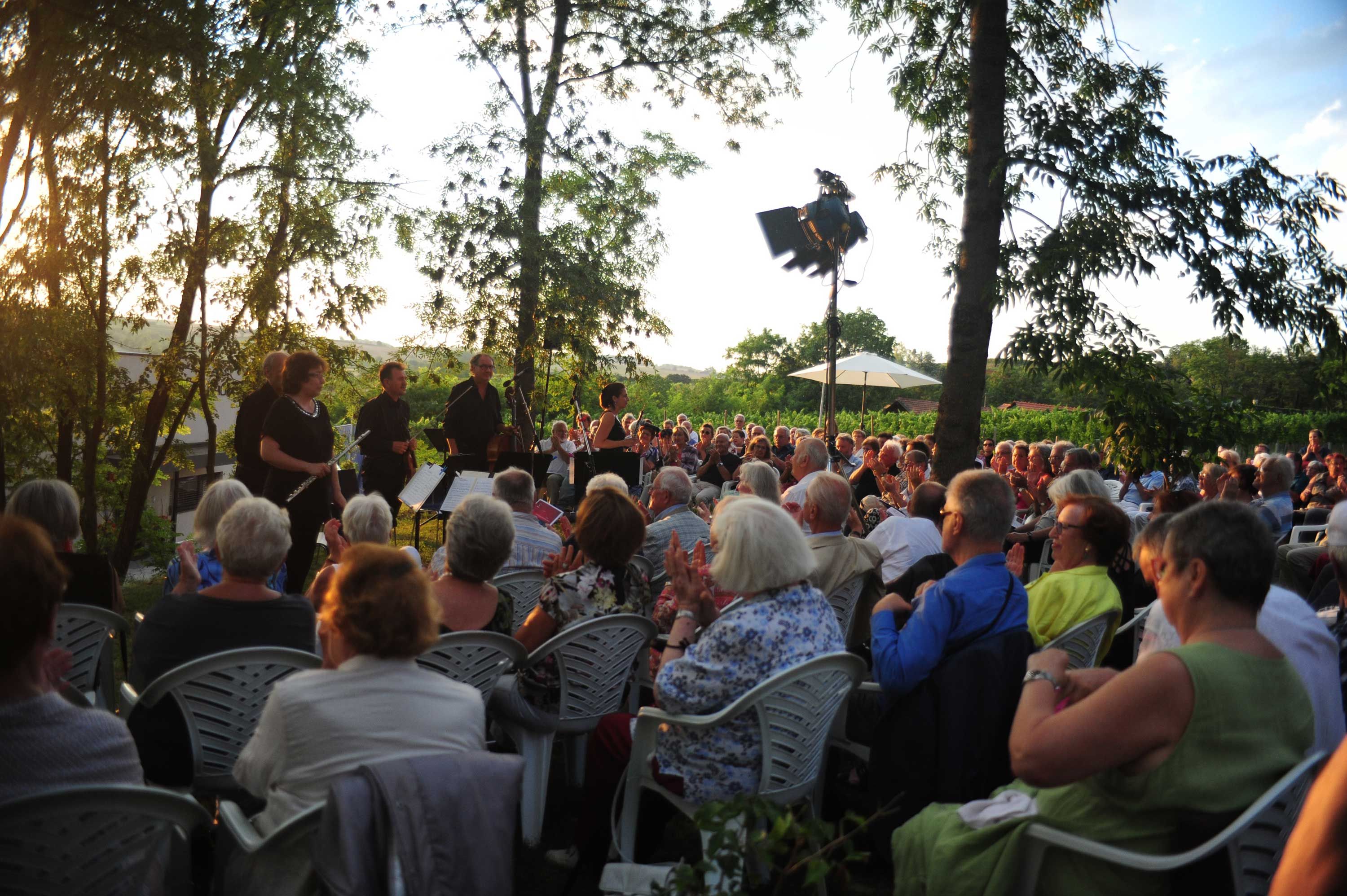 Ein Konzert im Freien mit einem Orchester und Publikum bei Sonnenuntergang.