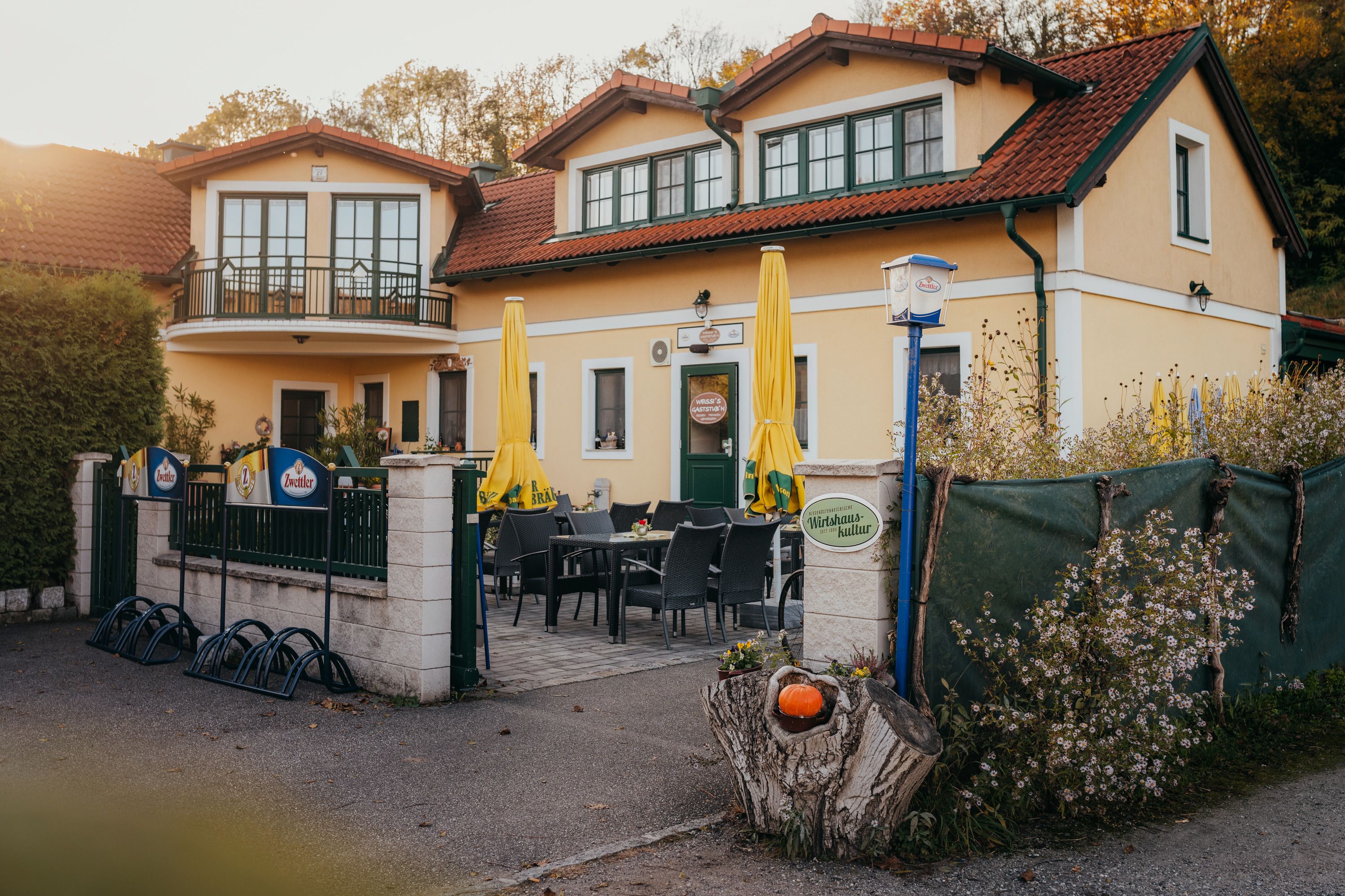 Gasthaus mit Terrasse, gelben Sonnenschirmen und Blumendekor.