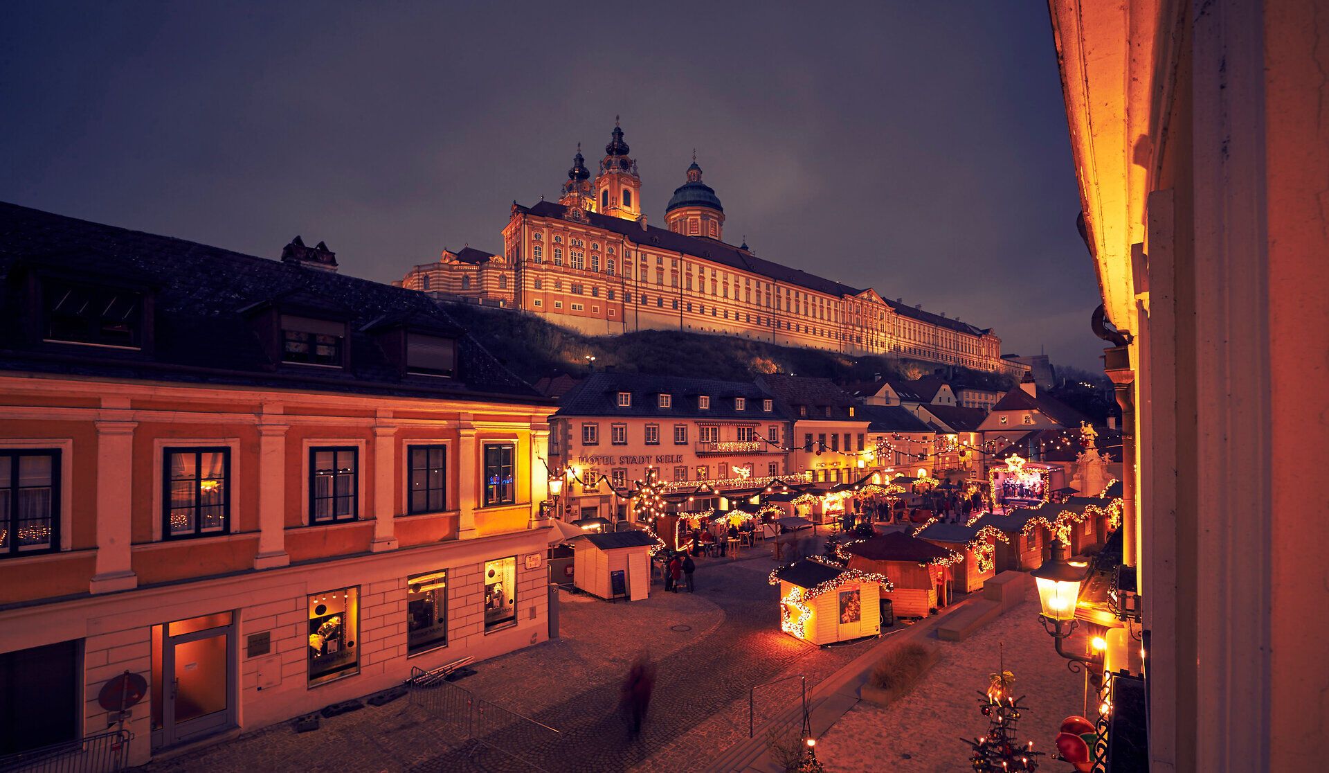 Stift Melk in der Dämmerung beleuchtet mit Adventhütten davor.