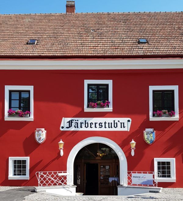 Red building with the inscription 'Färberstub'n' and blooming flowers in the windows.