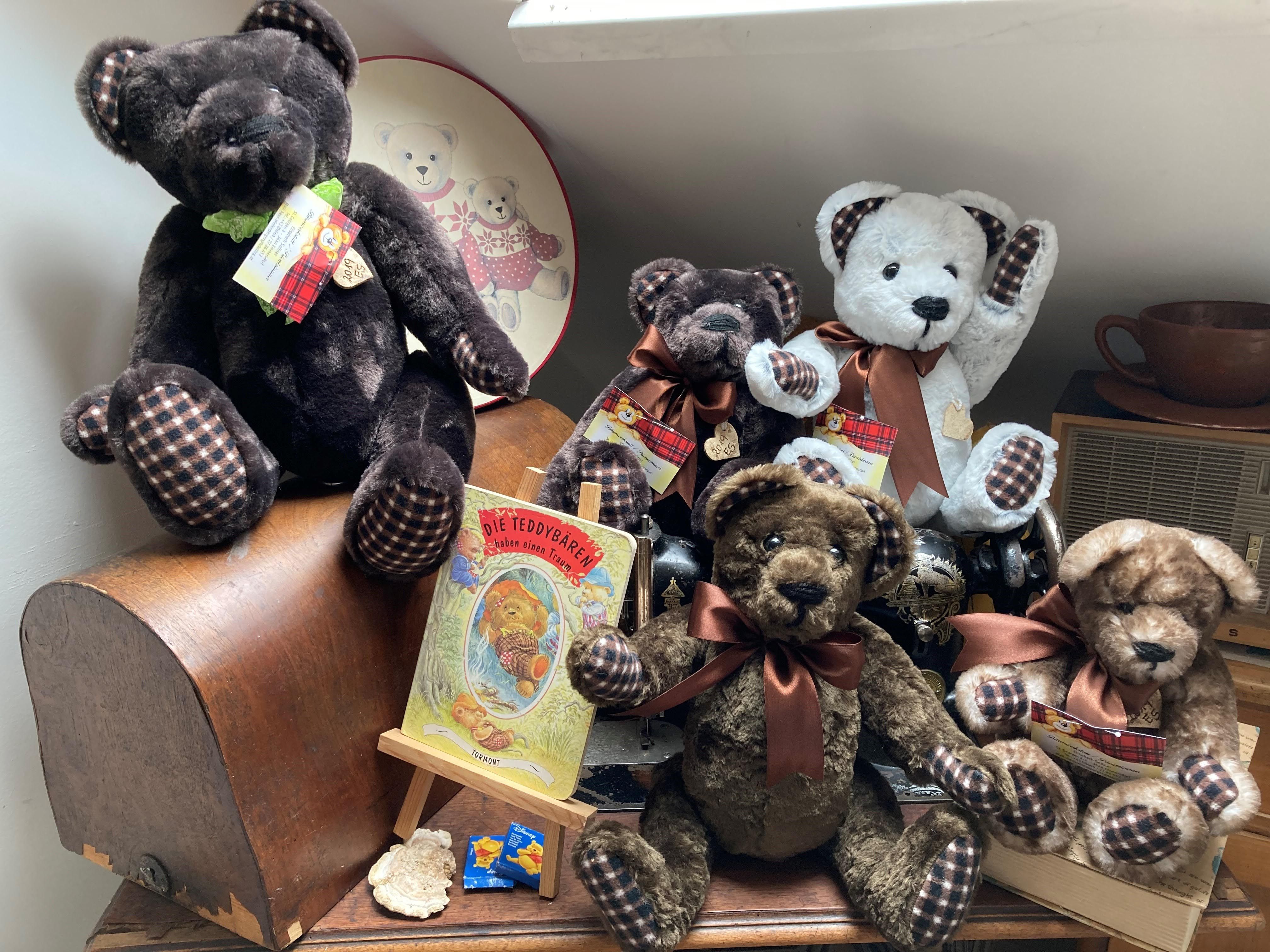 Eine Sammlung von Teddybären auf einem Tisch, umgeben von Dekorationen und einem Buch über Teddybären.