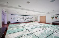 Ein großer Raum mit einem hellen Fußboden, der die Riedenkarte zeigt, im Hintergrund eine große Tafel mit dem Schriftzug Winzer Krems.