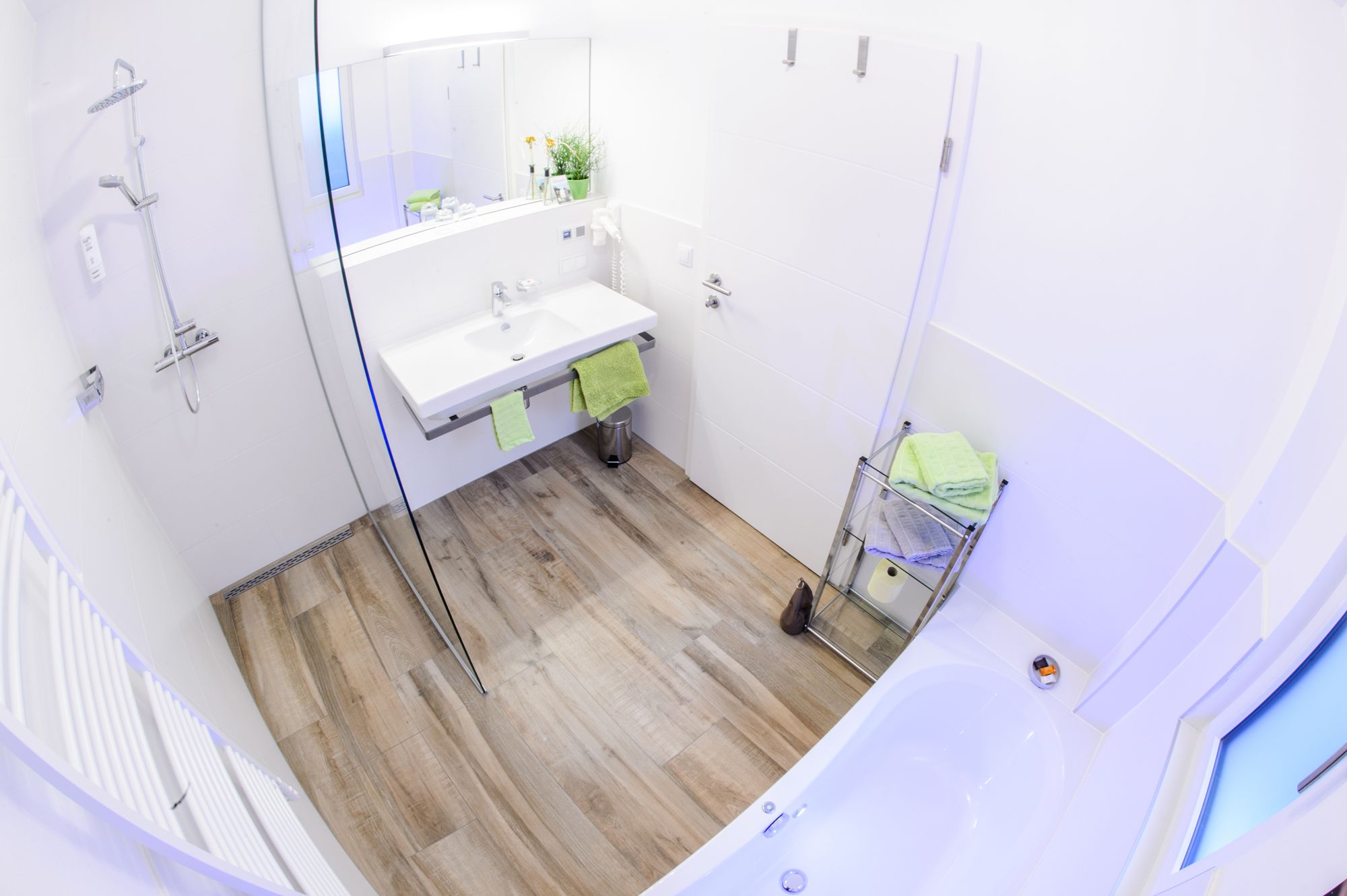 Modernes Badezimmer mit Dusche, Waschbecken und Badewanne, dekoriert mit grünen Handtüchern.