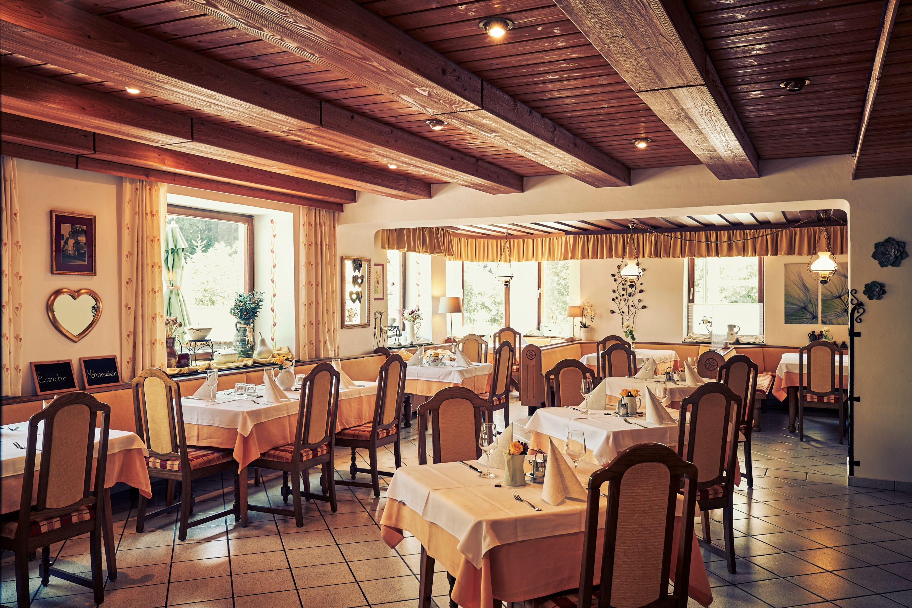 Gemütliches Restaurant mit Holzbalkendecke und gedeckten Tischen.