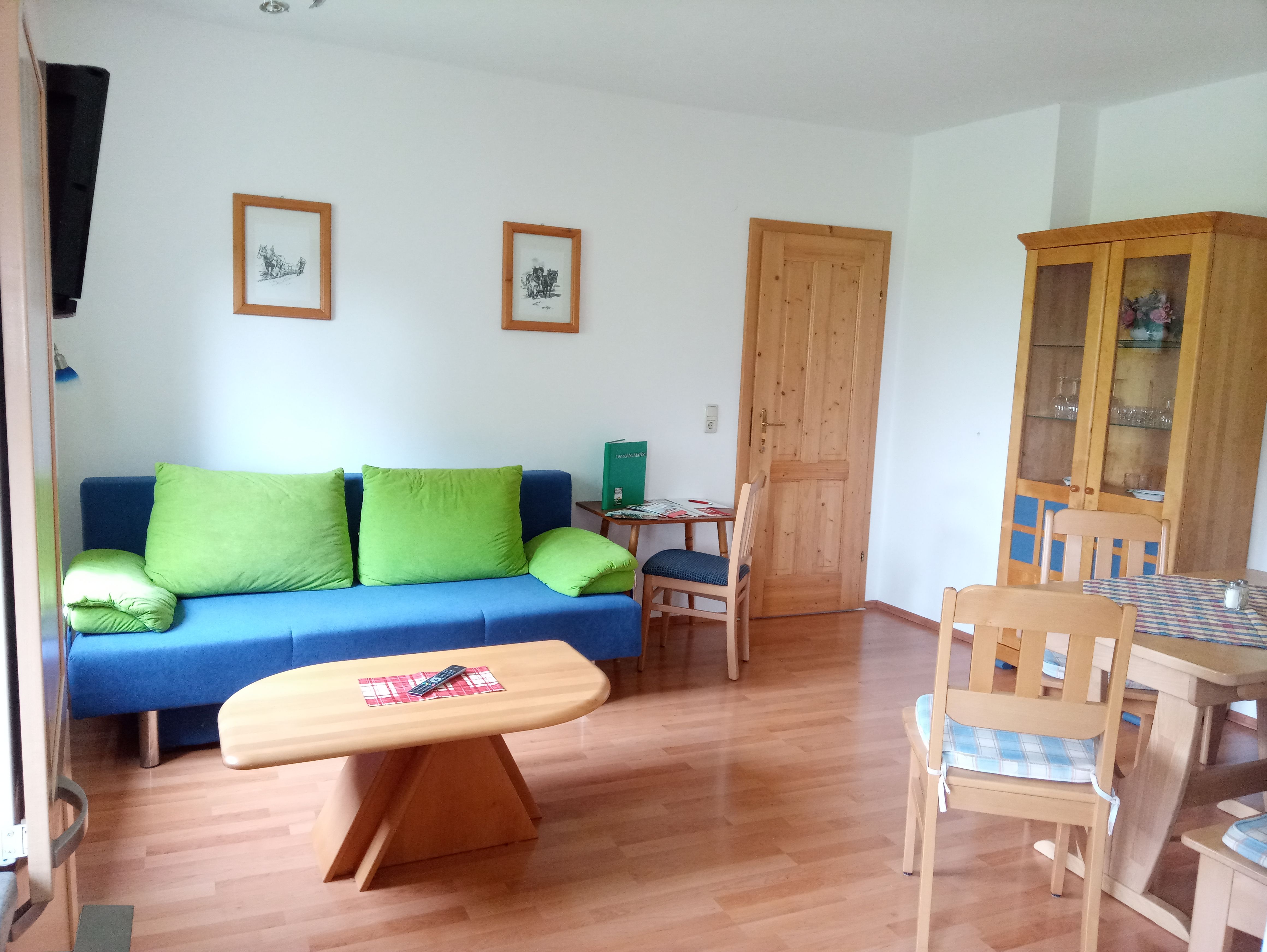 Wohnzimmer mit blauer Couch, Holztisch und Stühlen, Schrank und Bildern an der Wand.