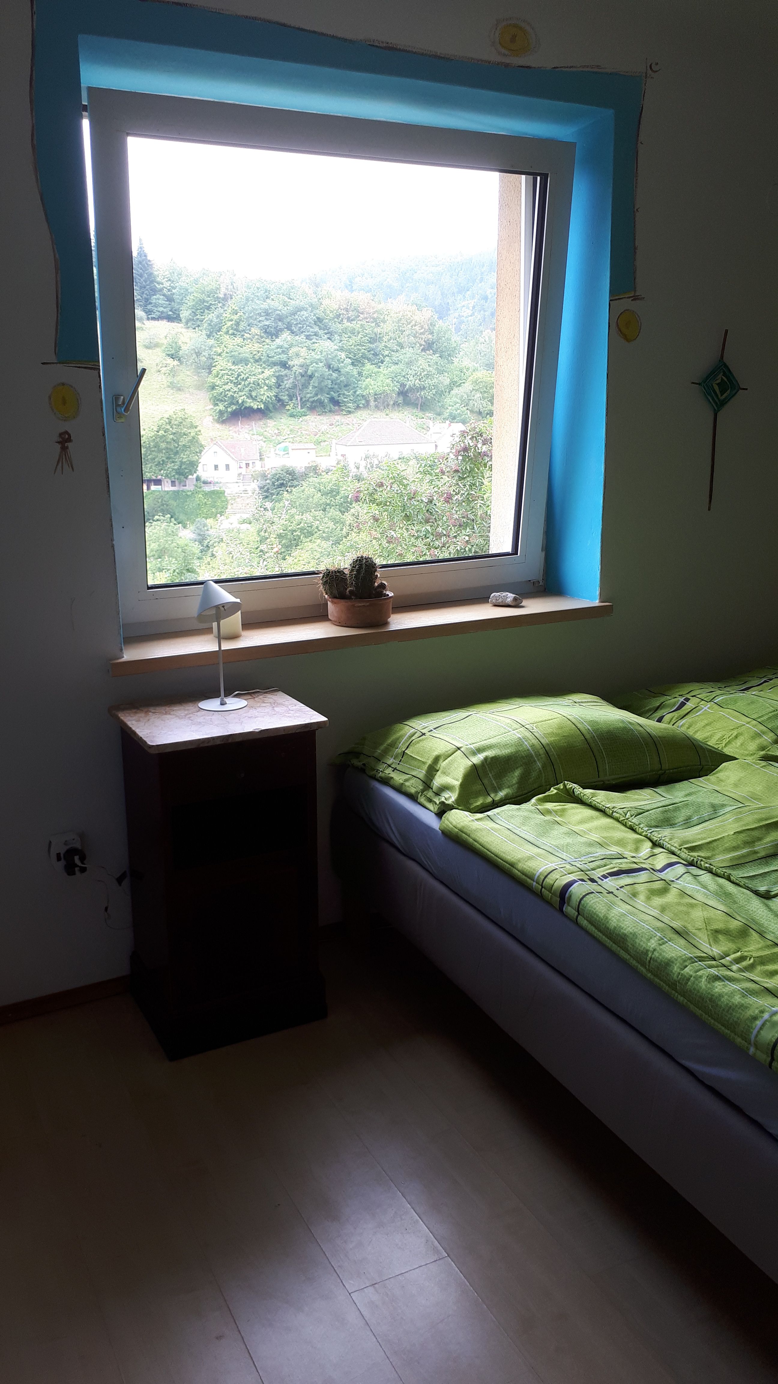 Ein Schlafzimmer mit einem Bett, einem Nachttisch und einem Fenster mit Blick auf eine grüne Landschaft.