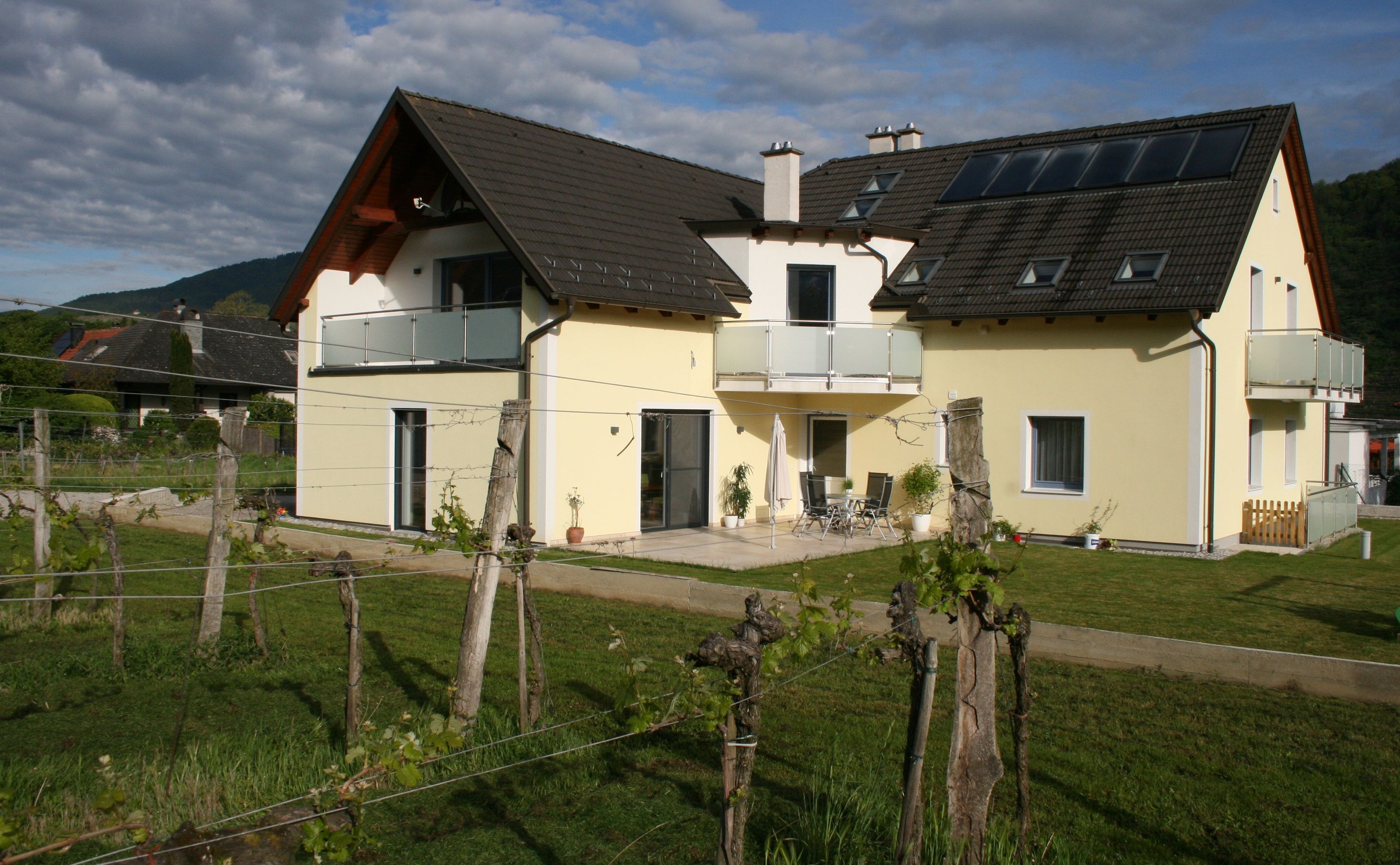 Gelbes Haus mit Balkon und Garten, umgeben von Weinreben.