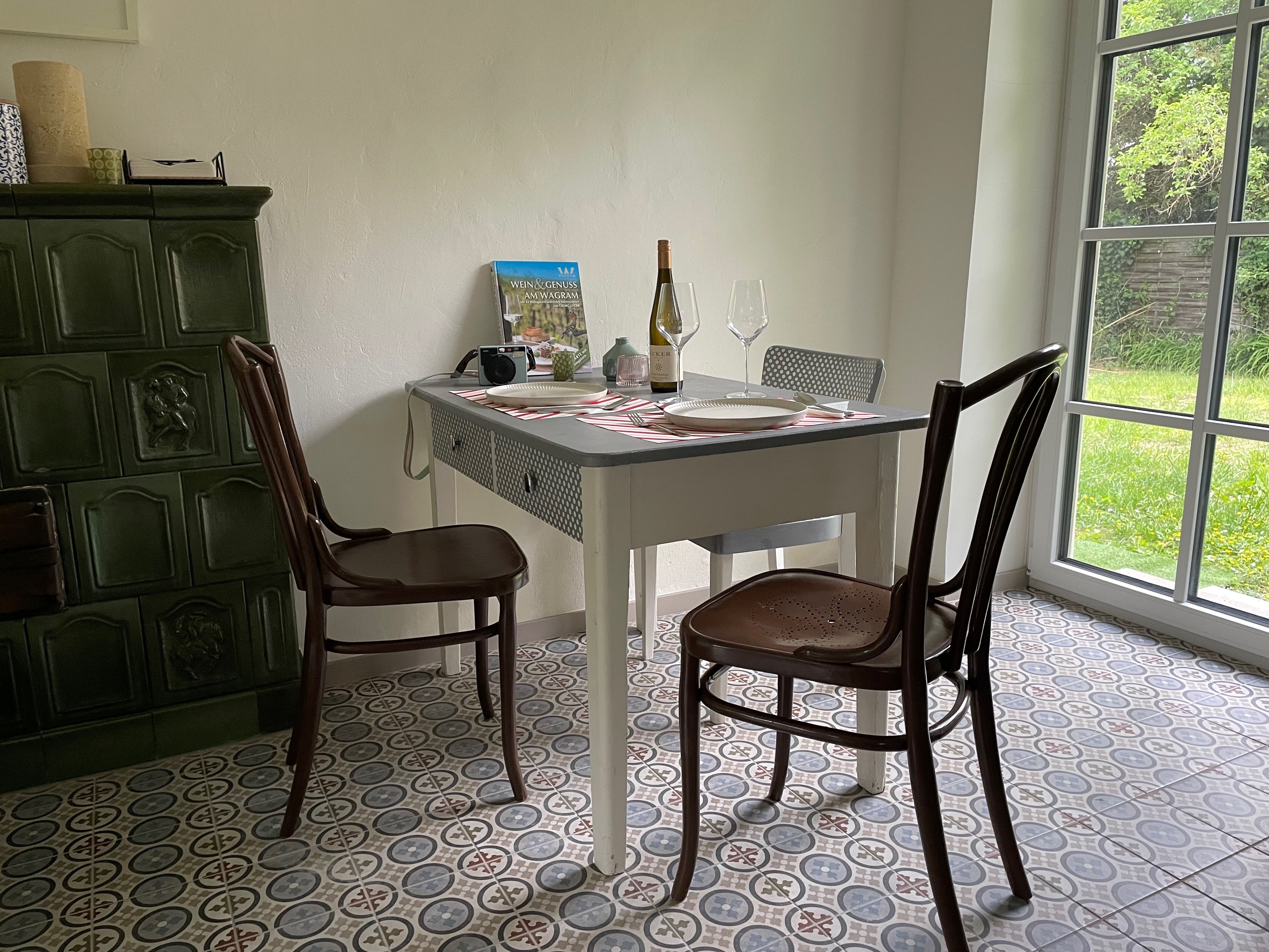 Gemütlicher Essbereich einer Ferienwohnung am Wagram mit regionalem Wein, historischem Kachelofen und Blick in den Garten.