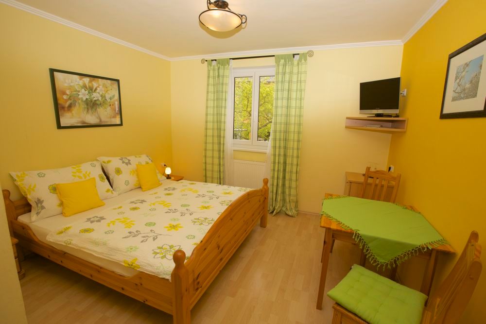 Gemütliches Gästezimmer mit Doppelbett, gelben Wänden und kleinem Tisch.