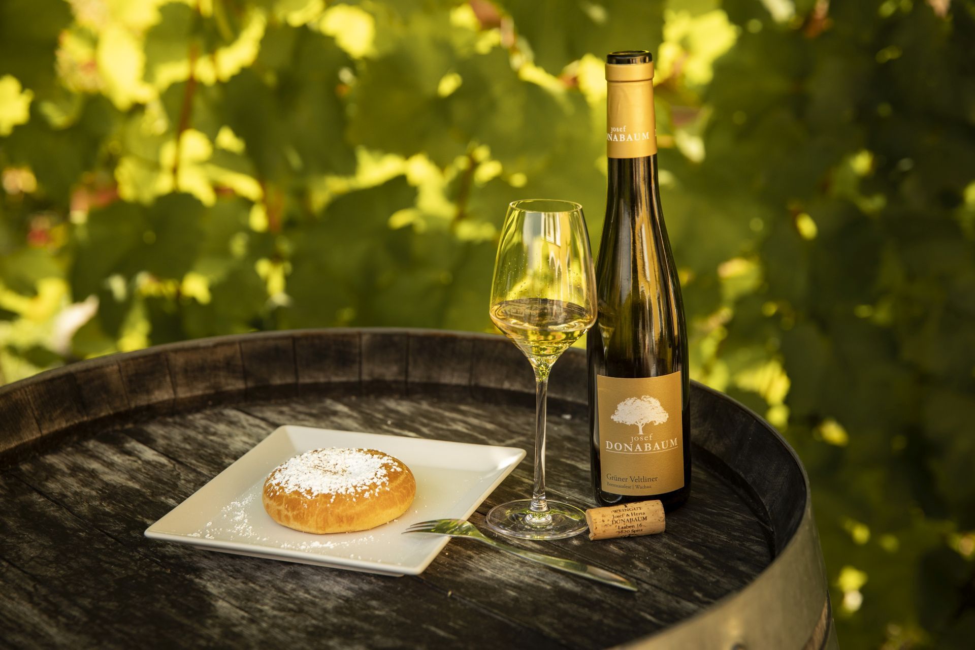 Weinflasche und Glas mit Gebäck auf einem Fass im Freien.
