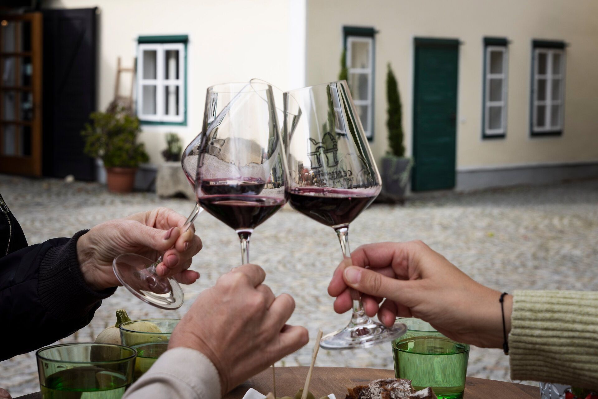 Drei Weingläser mit Rotwein stoßen an, zu sehen sind nur die Hände.