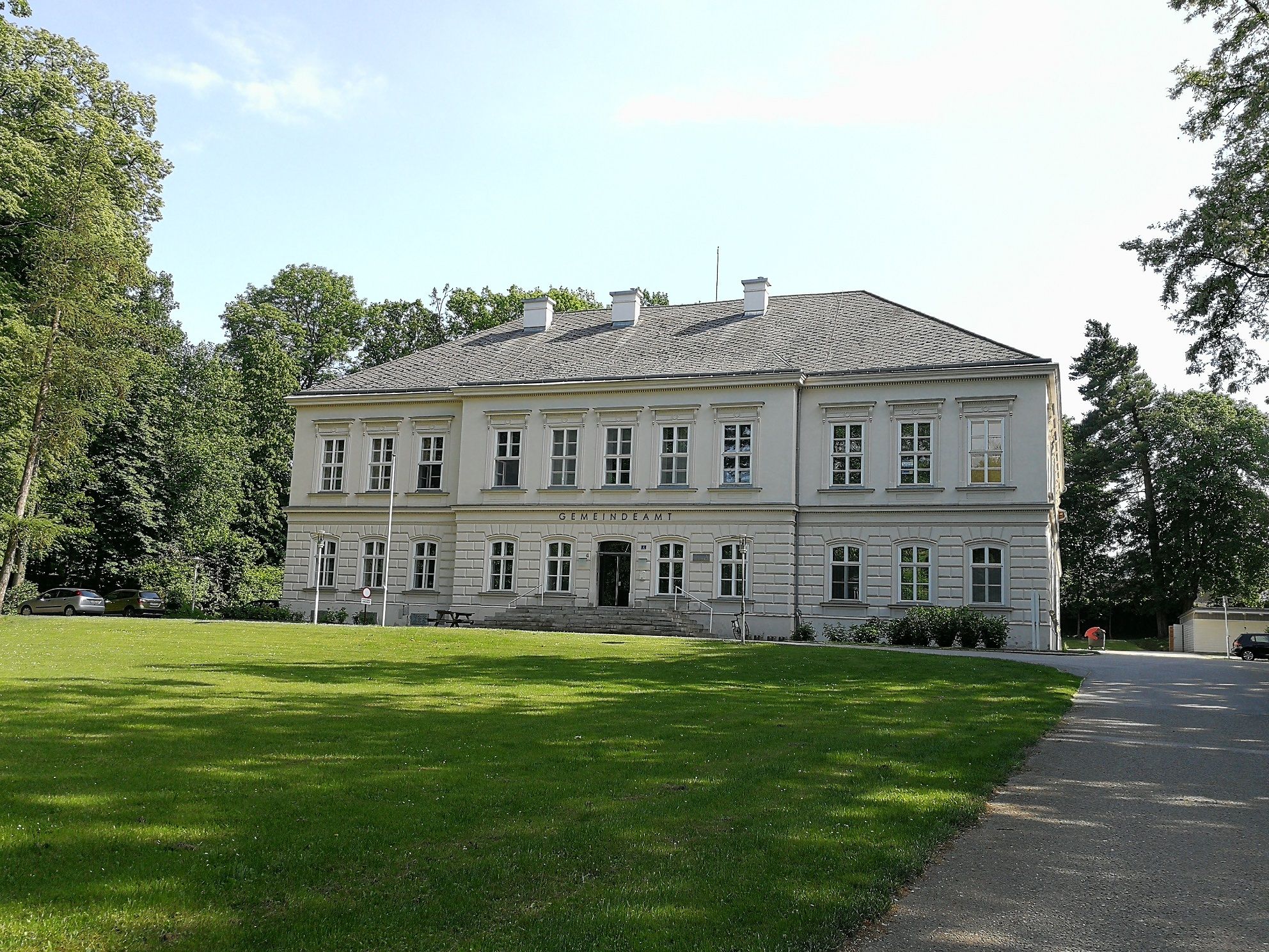 Schloss Würmla, ein zweistöckiges Gebäude mit grauem Dach und weißen Wänden, umgeben von Bäumen und Rasen.