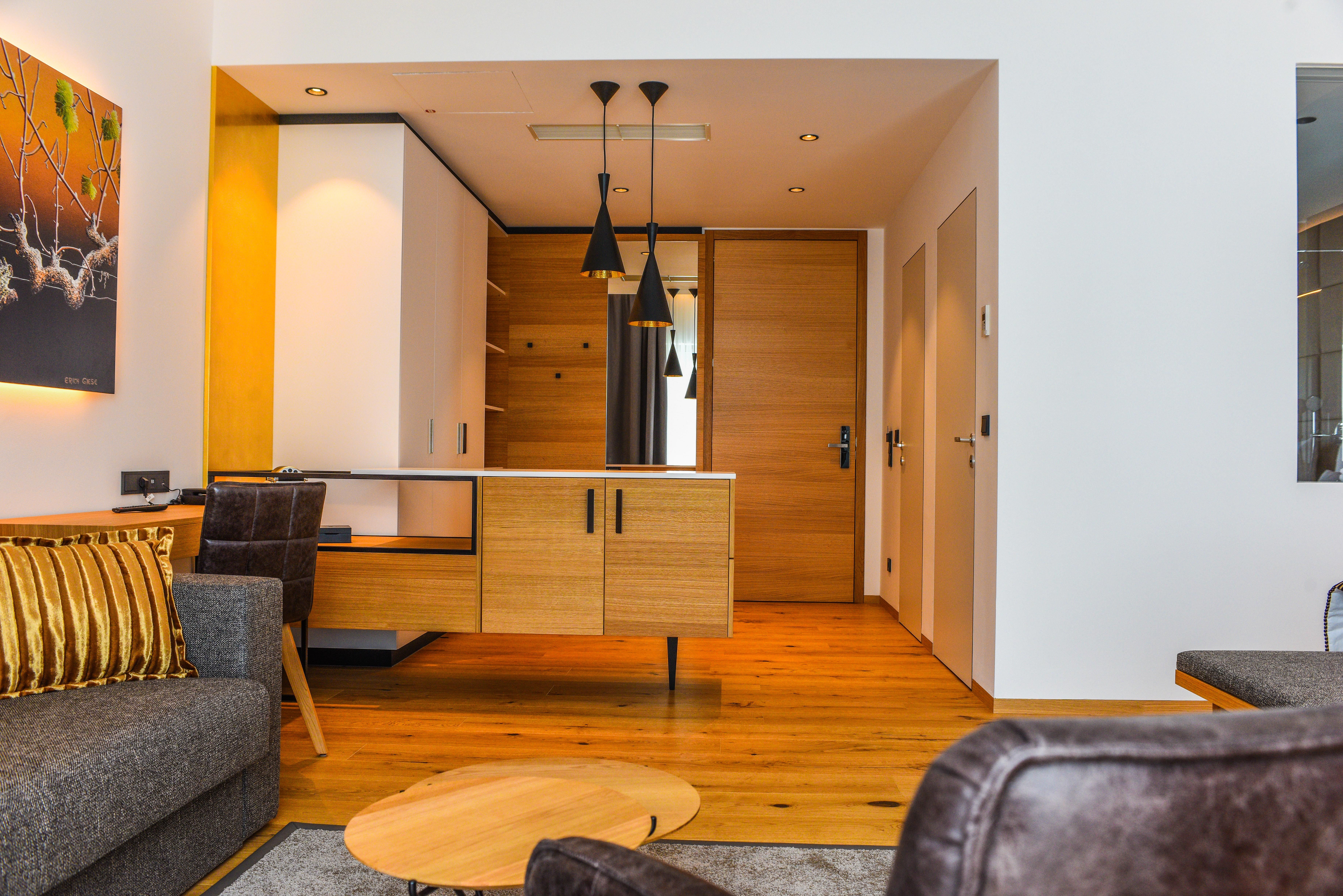 Innenansicht einer modernen Hotelsuite mit Holzboden, grauem Sofa und hölzernem Schreibtisch.