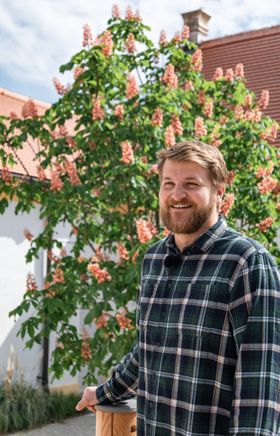 Der Abteilungsleiter Garten von Schloss Hof, Sebastian Joos, steht in einem kariertem Hemd vor einem blüehendem Baum.