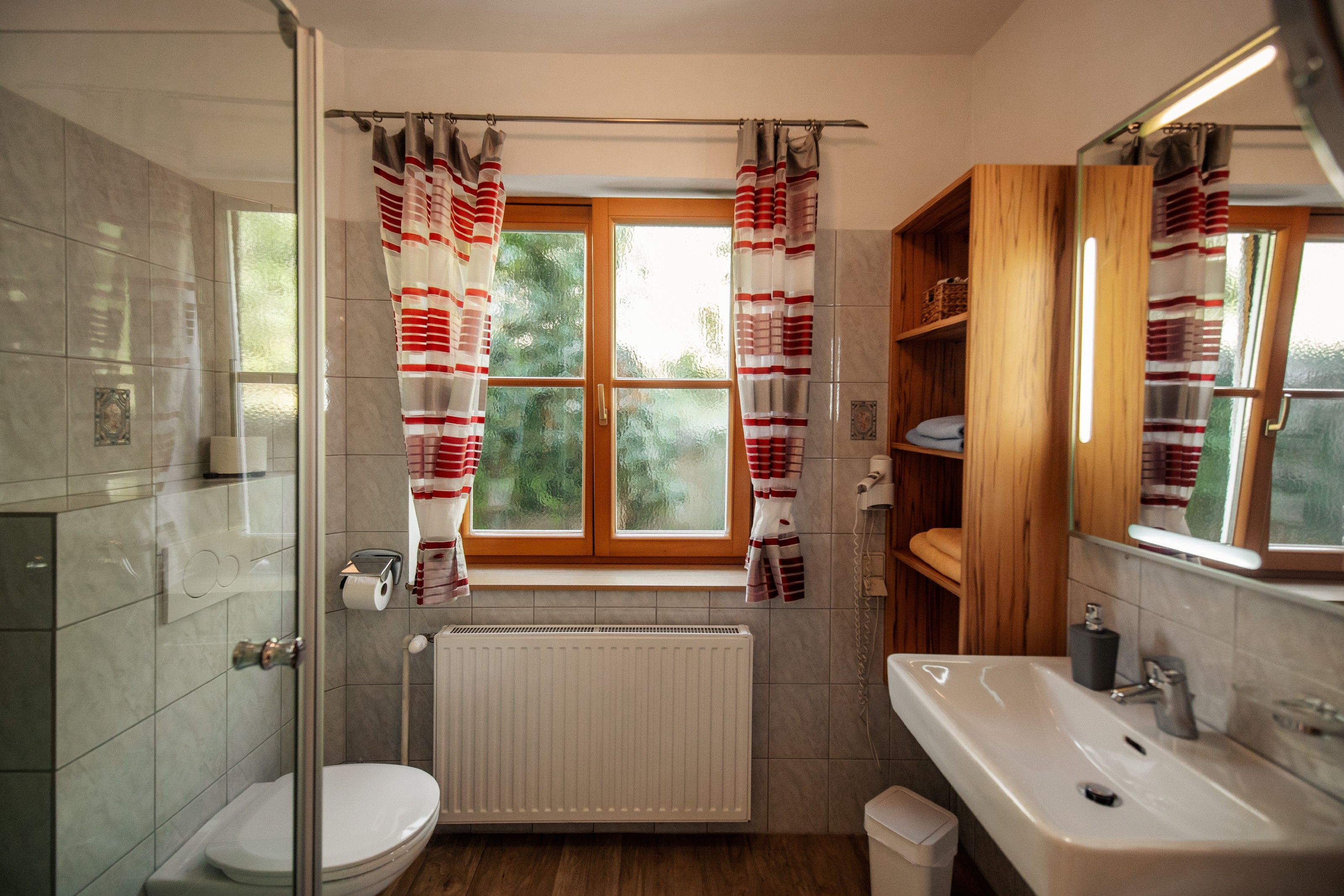 Modernes Badezimmer mit Fenster, Duschkabine, Waschbecken und Regalen.