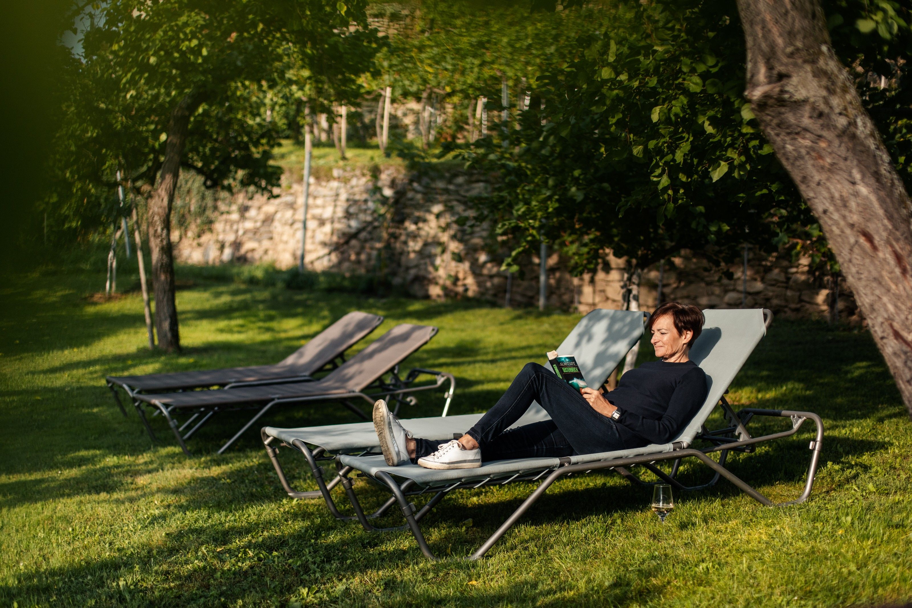 Person liest auf einer Sonnenliege im Garten.