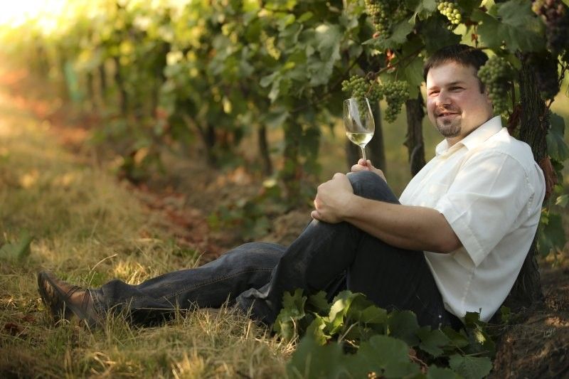Mann sitzt im Weingarten mit einem Glas Weißwein.