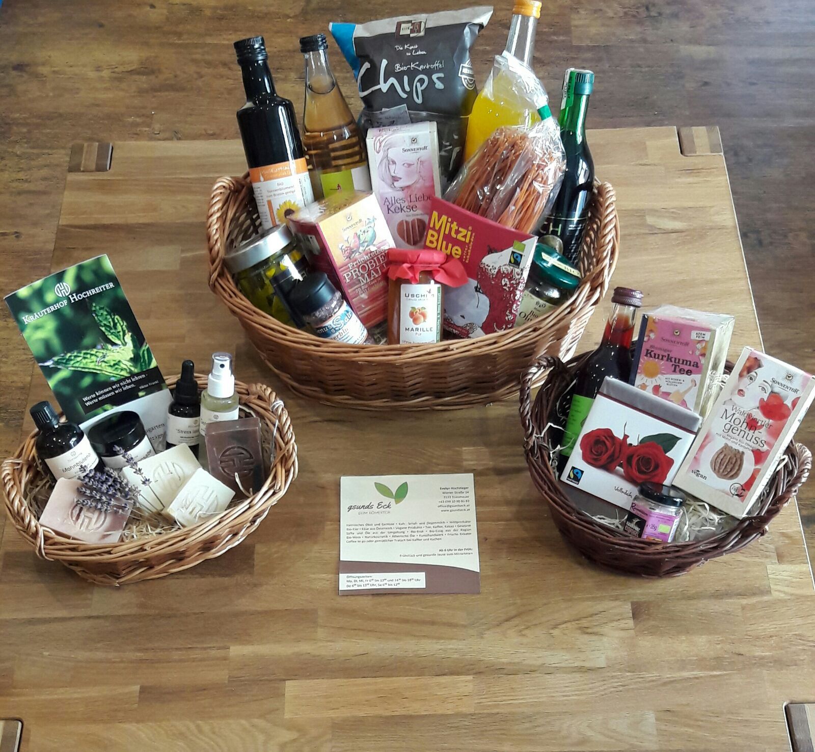 Drei gefüllte Geschenkkörbe auf einem Holztisch.