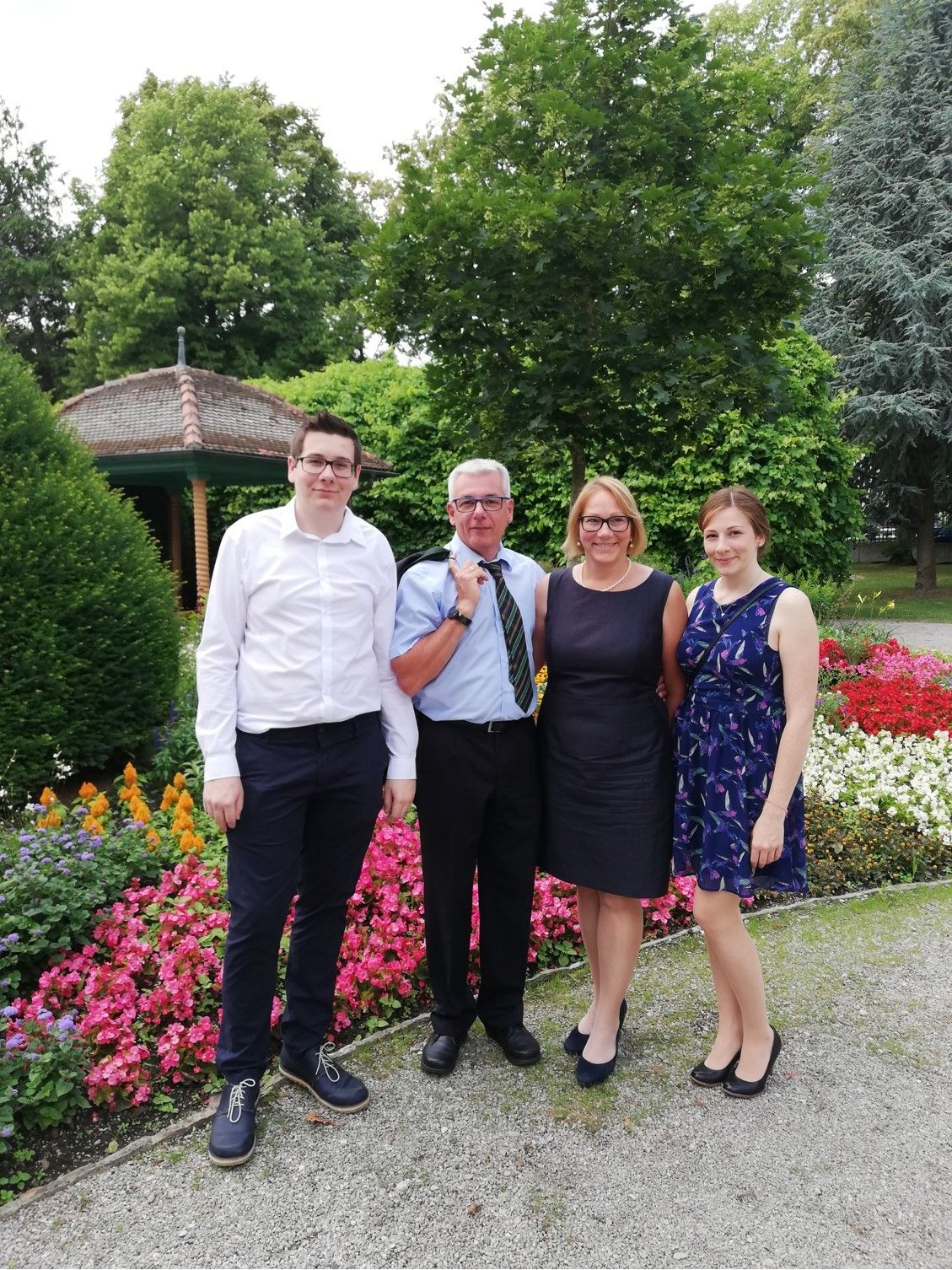Vier Personen stehen vor einem Blumenbeet im Freien.