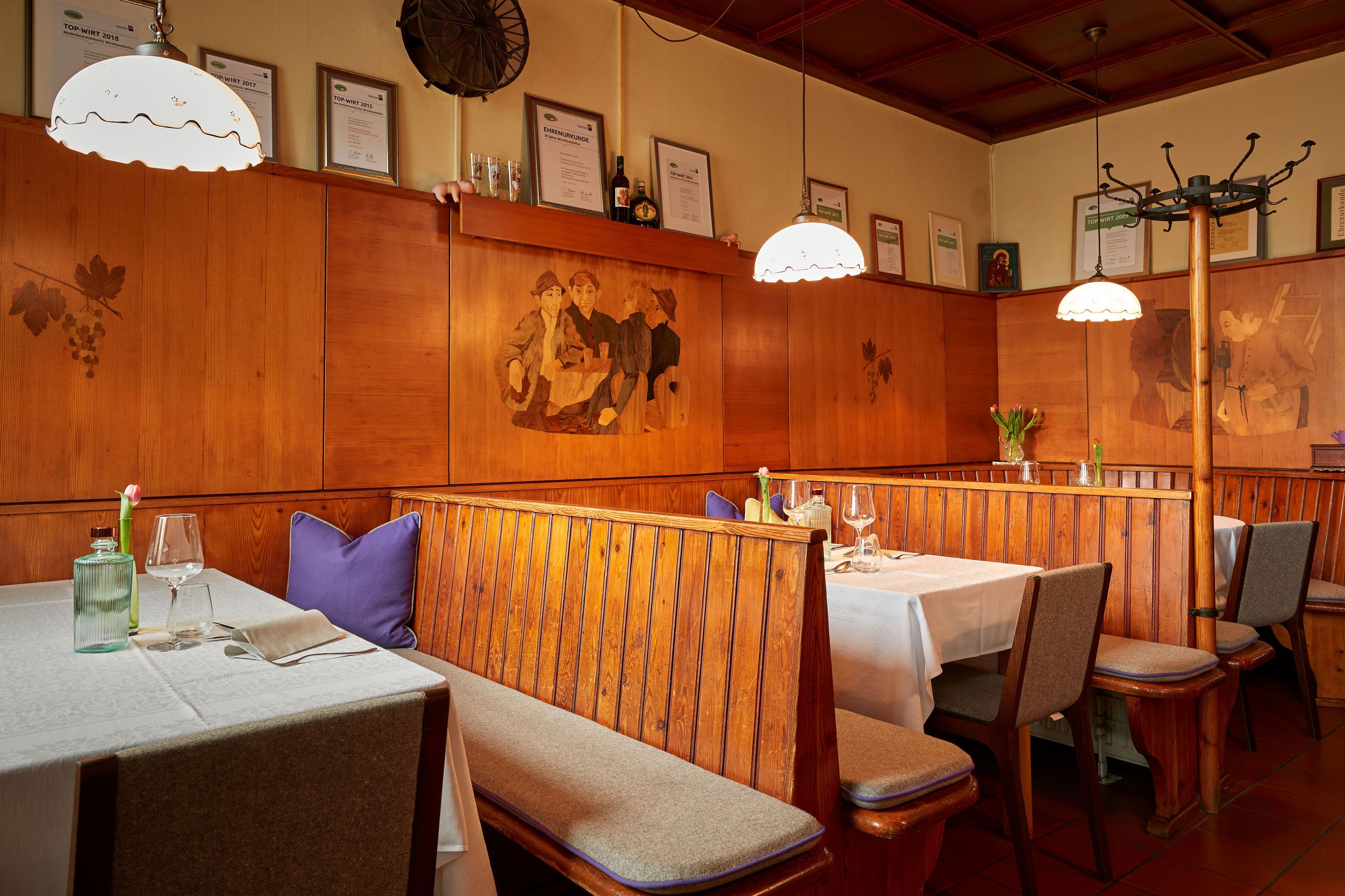 Gemütliches Restaurant mit Holzbänken, Tischdecken und Wanddekorationen.