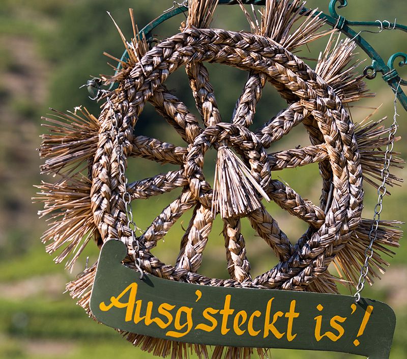 Ein geflochtener Strohkranz mit dem Schild 'Ausg'steckt is!' hängt an einer Kette.