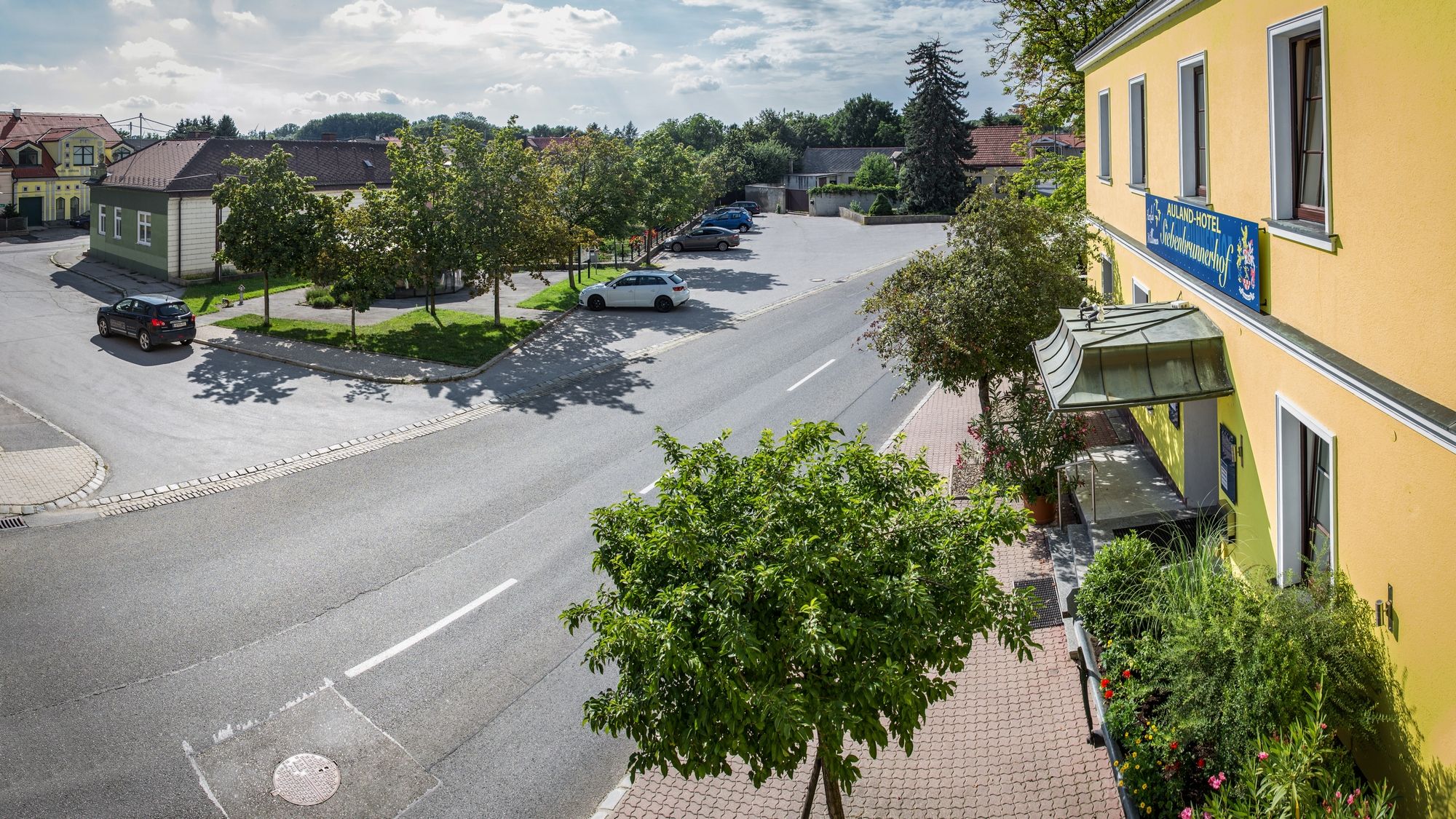Street scene with yellow building and parking lot, trees and cars.