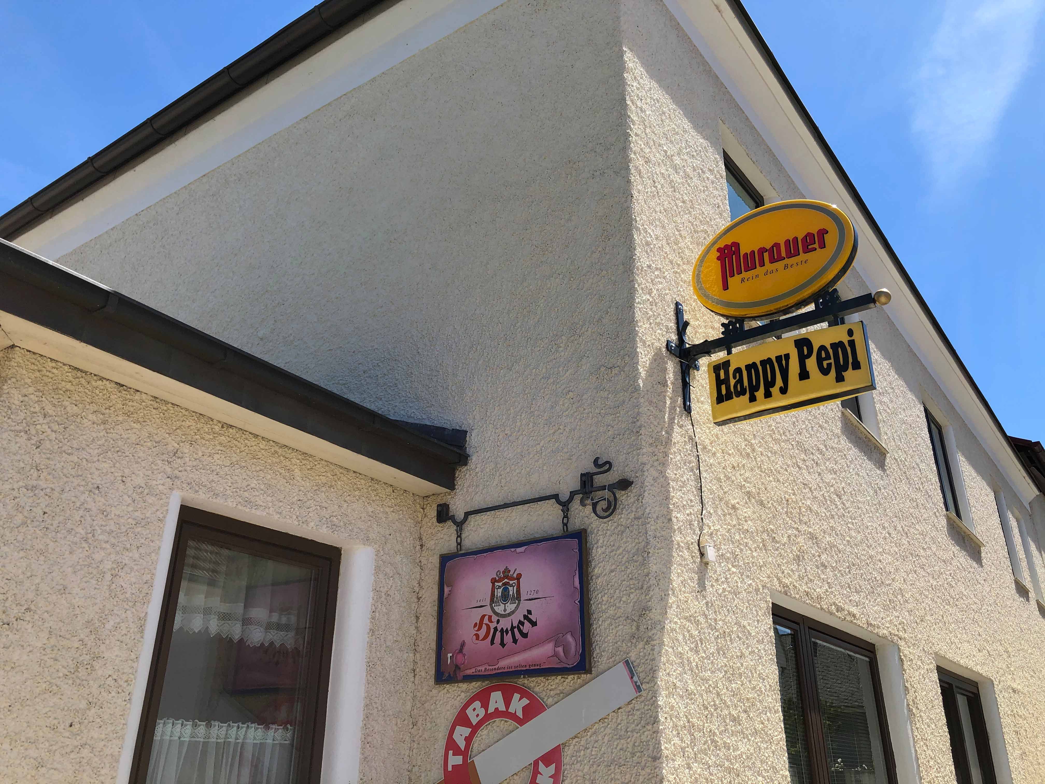 Außenansicht eines Gebäudes mit Schildern von 'Murauer' und 'Happy Pepi'.