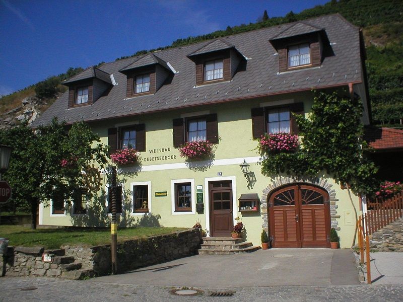 Außenansicht eines Weinguts mit gelber Fassade und Blumen.