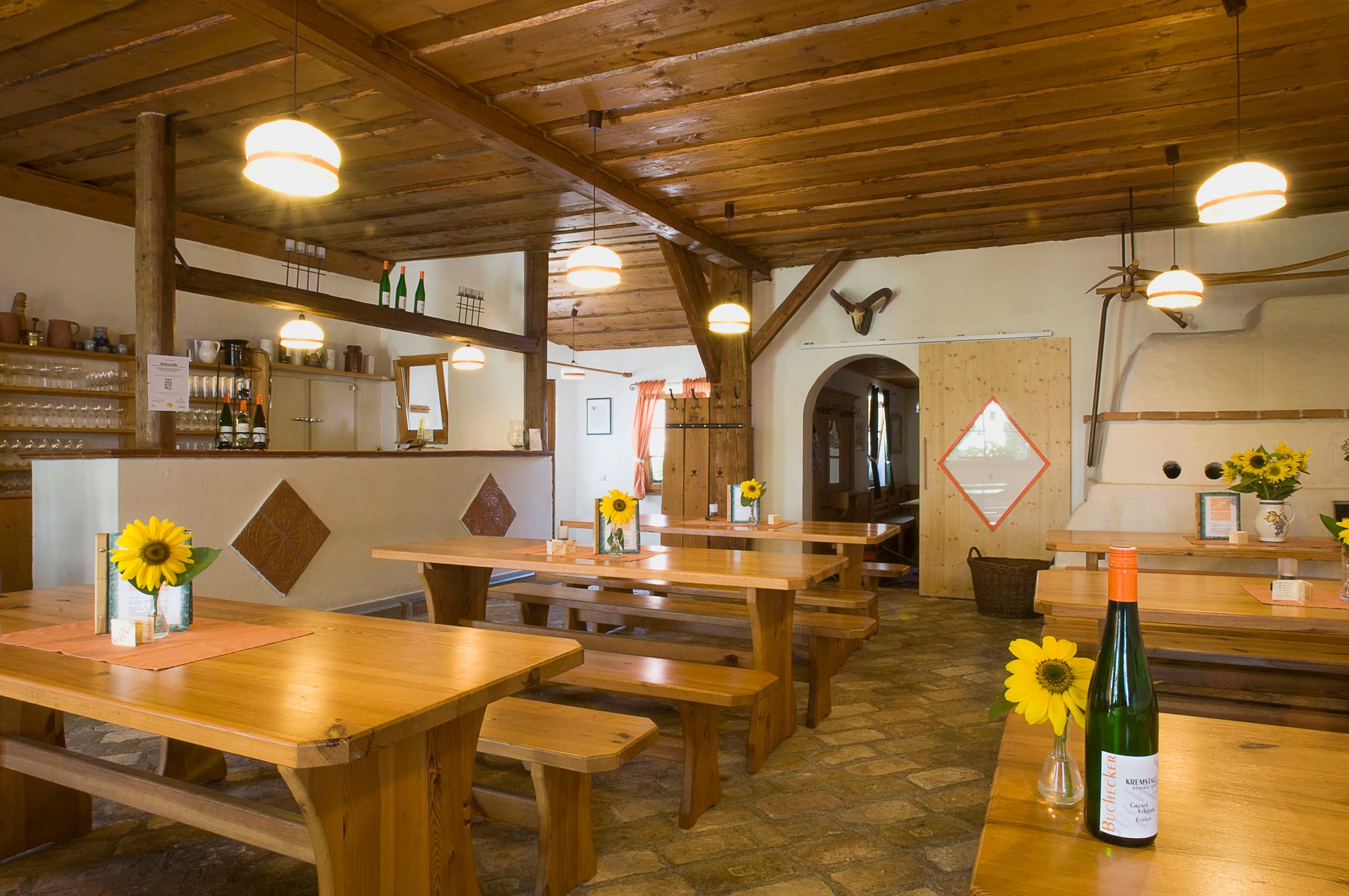 Innenansicht eines traditionellen Heurigenlokals mit Holztischen, Sonnenblumen und Weinflaschen.