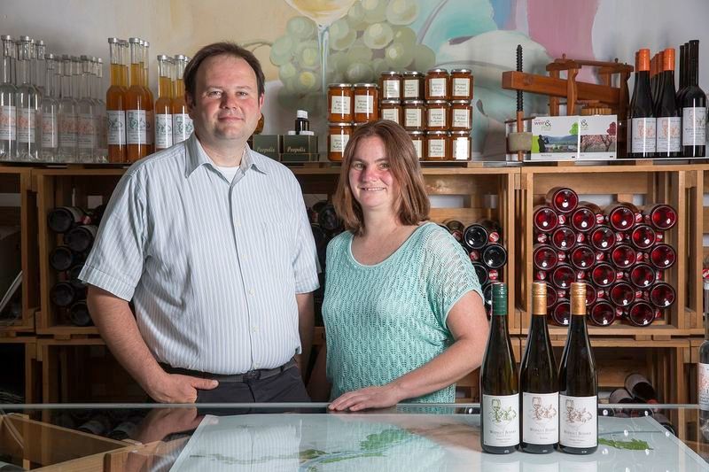 Zwei Personen stehen in einem Weingut vor Weinflaschen und Regalen mit Produkten.