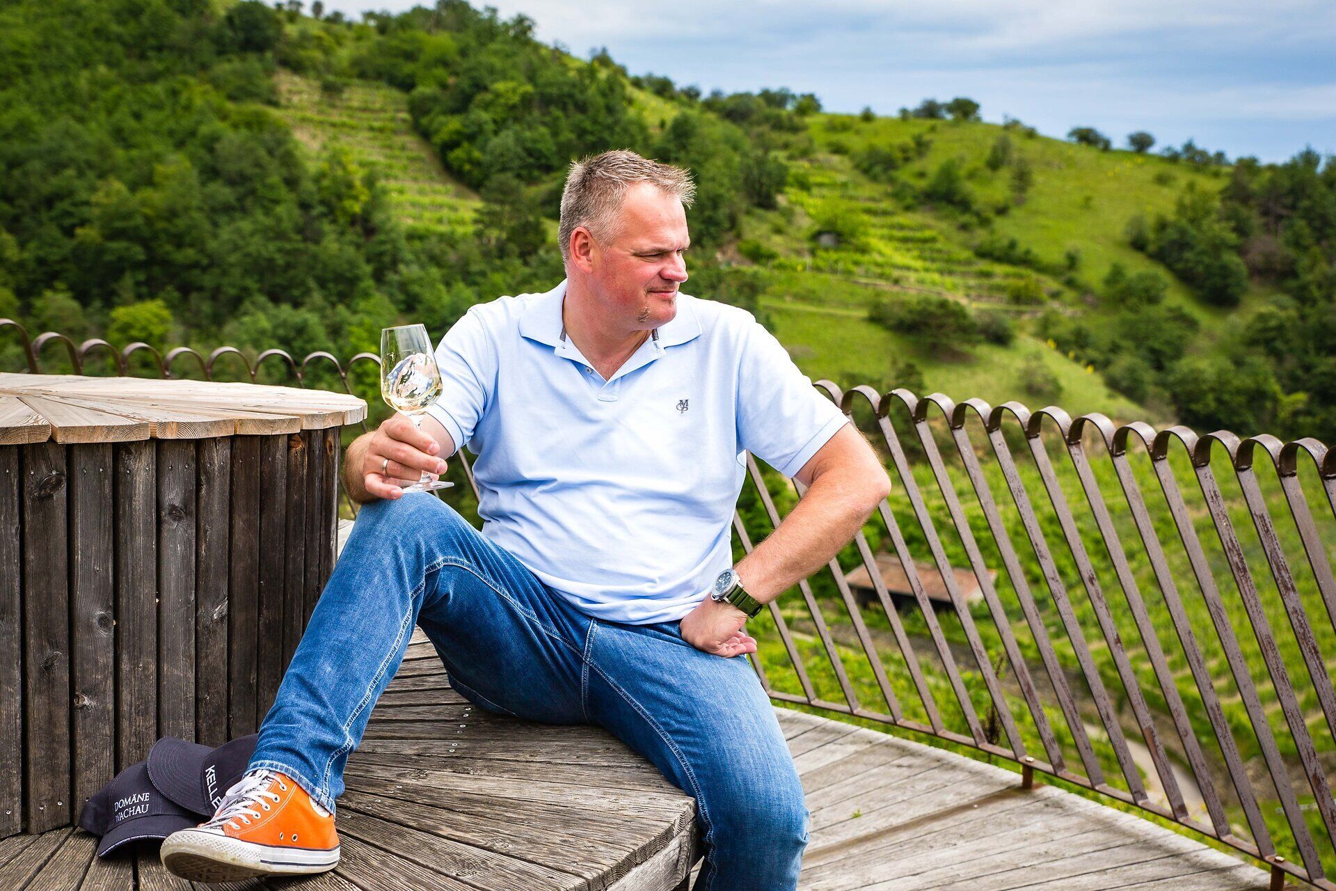 An einer malerischen Aussichtsplattform genießt man den Sommer in vollen Zügen. Umgeben von sanften Hügeln und üppigen Weinreben, strahlt die Atmosphäre Ruhe und Genuss aus. Ein Glas erlesener Wein in der Hand lädt dazu ein, die atemberaubende Landschaft zu bewundern.