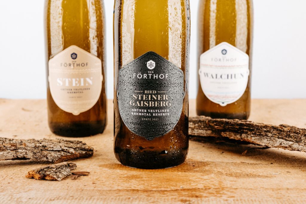 Drei Weinflaschen der Marke Förthof auf einem Holztisch mit Rindenstücken.